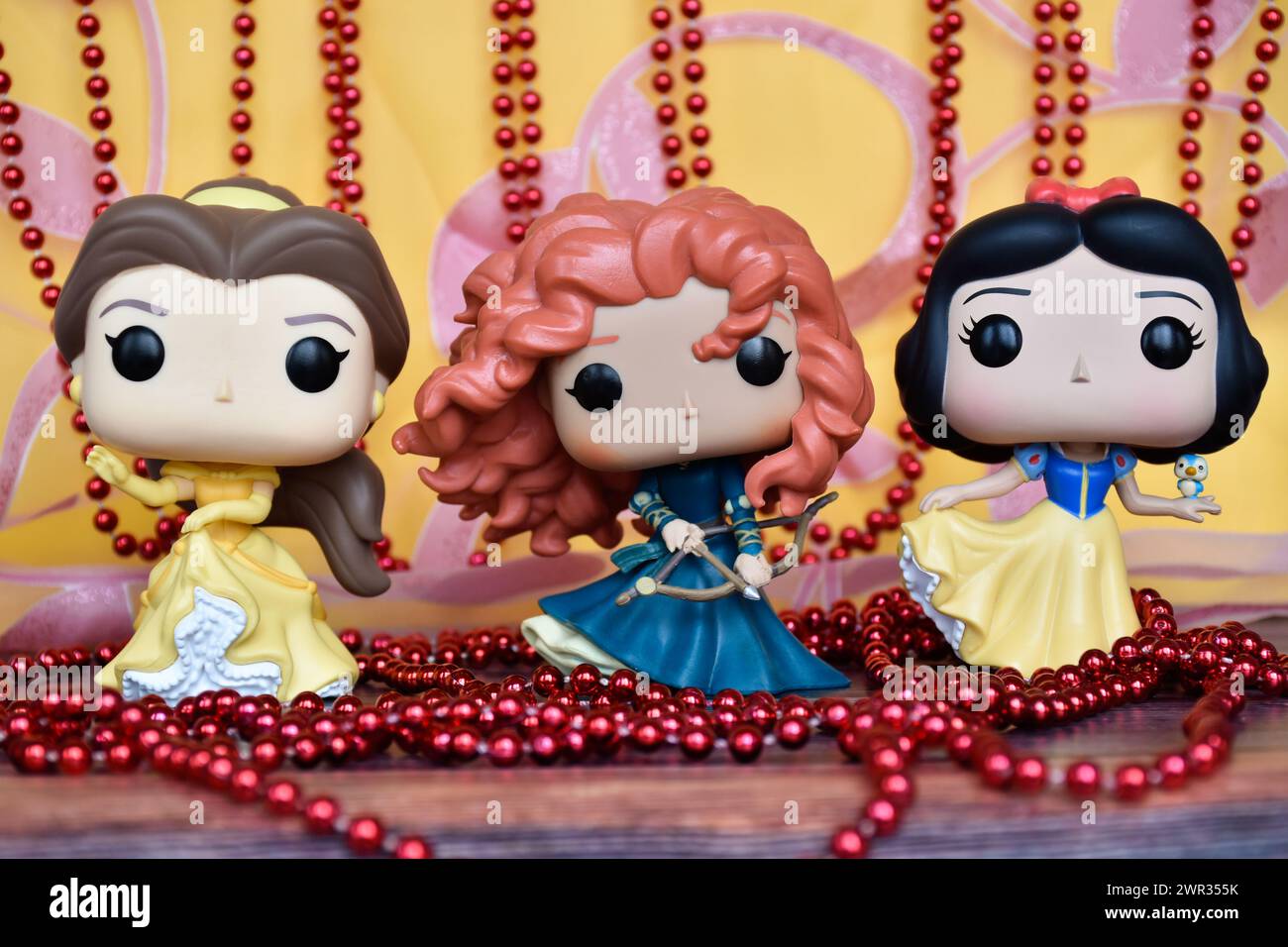 Funko Pop Actionfiguren der Disney-Prinzessinnen Belle (die Schönheit und das Biest), Merida (tapfer) und Schneewittchen. Goldener rosa Vorhang, rote Halskette, fabelhaft. Stockfoto