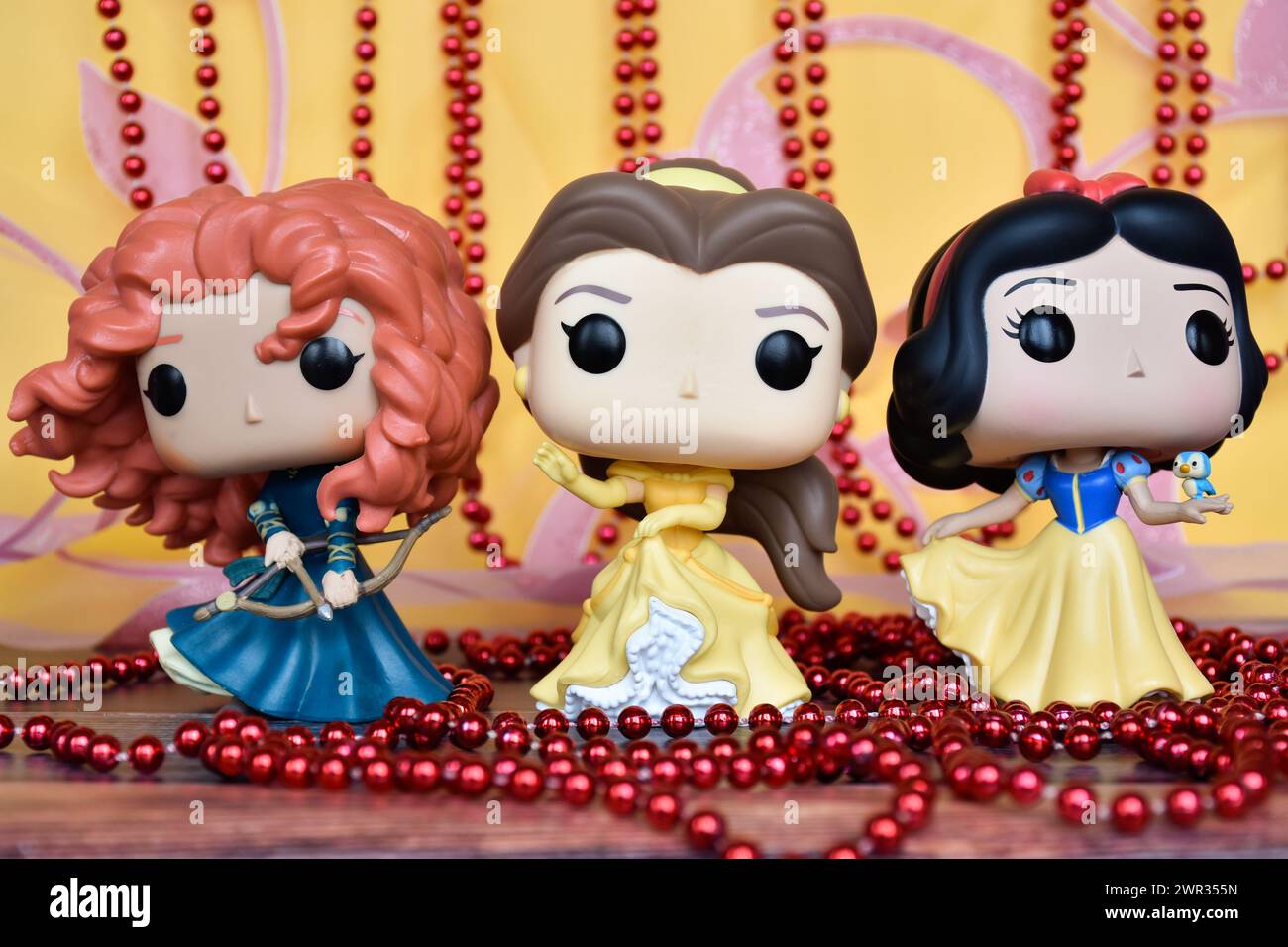 Funko Pop Actionfiguren der Disney-Prinzessinnen Merida (tapfer), Belle (Schönheit und das Biest) und Schneewittchen. Goldener rosa Vorhang, rote Halskette, fabelhaft. Stockfoto
