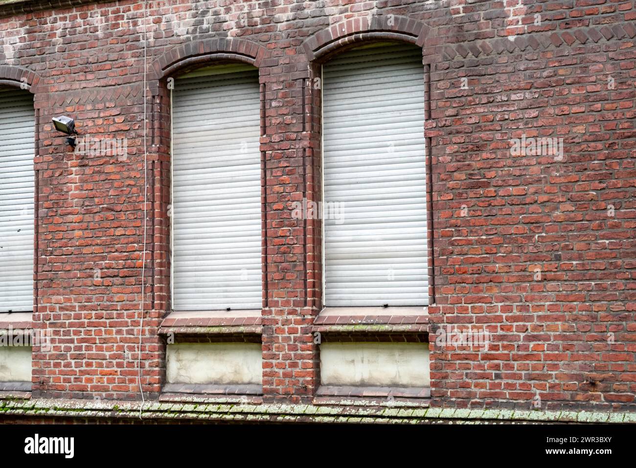 Drei gleichmäßig verteilte Fenster mit geschlossenen weißen Fensterläden in einer roten Ziegelwand Stockfoto