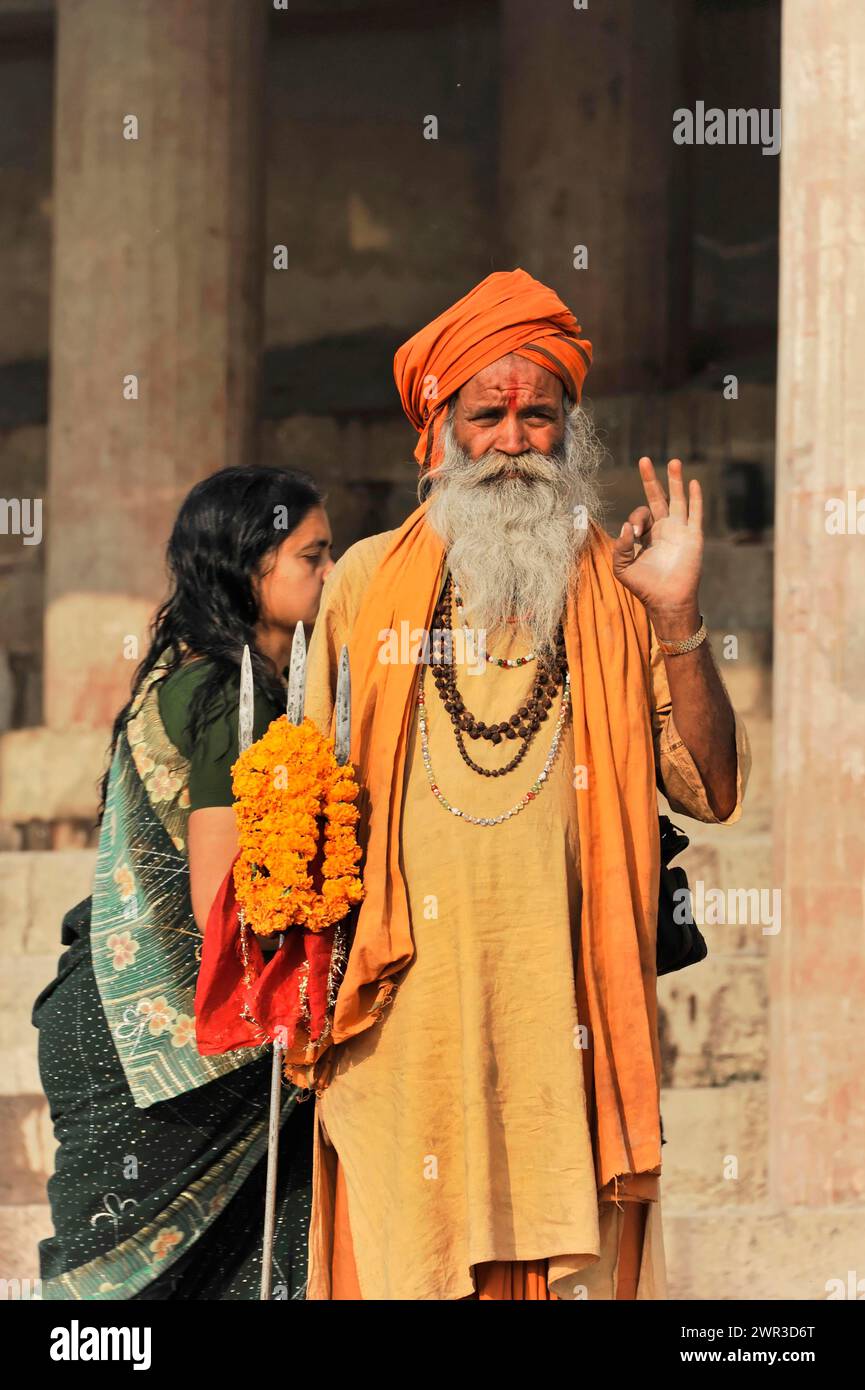 Mann in orangefarbener traditioneller Kleidung segnet Frau mit Blumenkranz, Varanasi, Uttar Pradesh, Indien Stockfoto