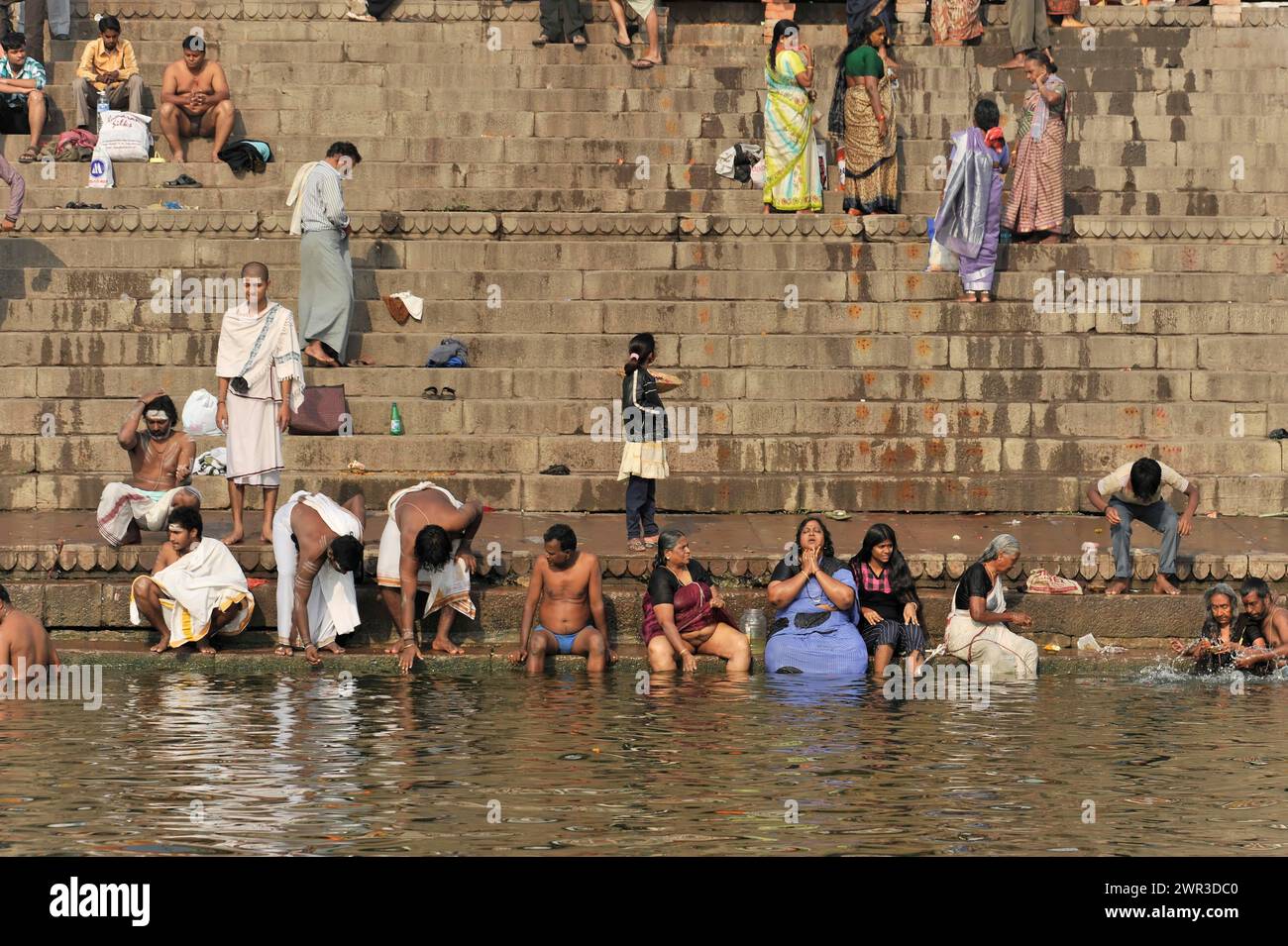 Menschen, die auf den Stufen eines Flusses baden und waschen, einige in traditioneller Kleidung, Varanasi, Uttar Pradesh, Indien Stockfoto
