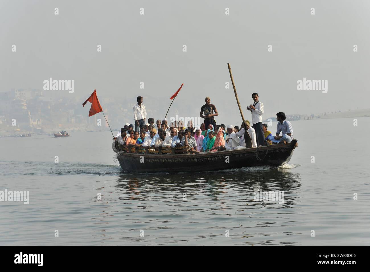 Gruppe von Passagieren auf einem Boot auf einem Fluss, mit einem Fährmann, der mit einem langen Ruder steuert, Varanasi, Uttar Pradesh, Indien Stockfoto