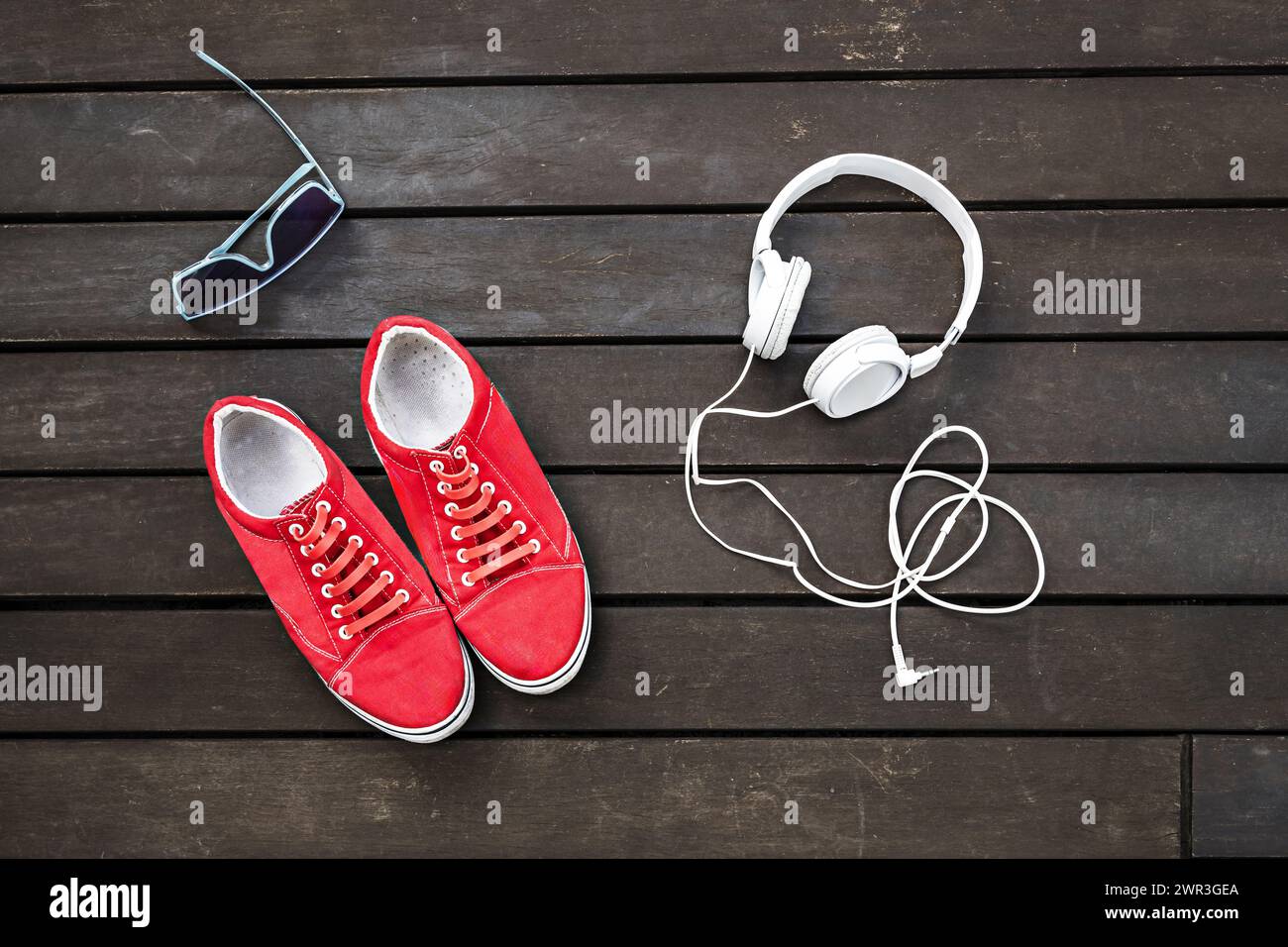 Rote Sneakers mit Kopfhörern und Sonnenbrille auf brauner Dielloberfläche Stockfoto