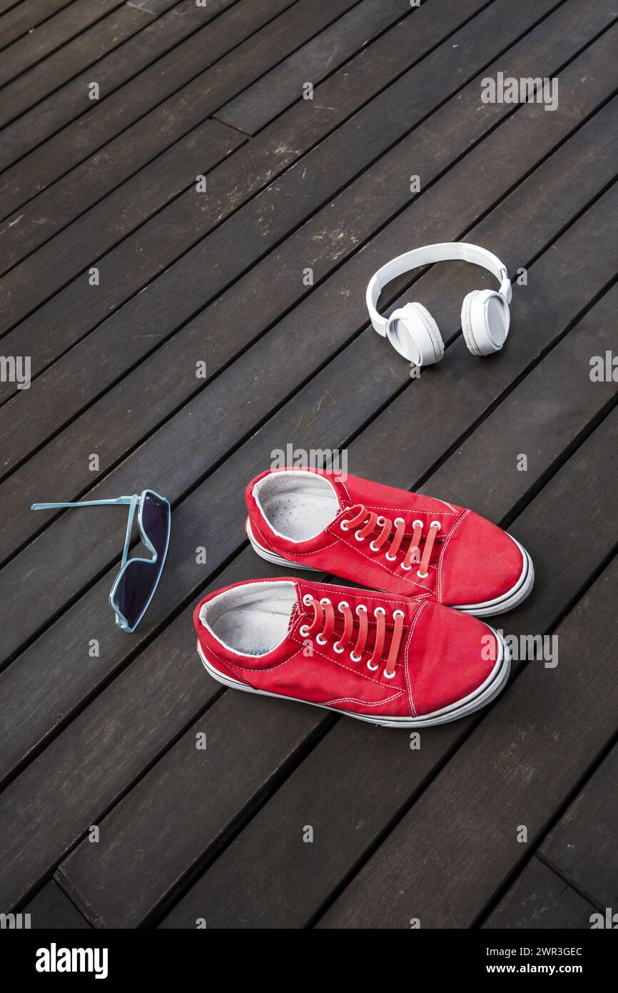Rote Sneakers mit Kopfhörern und Sonnenbrille auf brauner Planke auf einer Penthouse-Terrasse Stockfoto