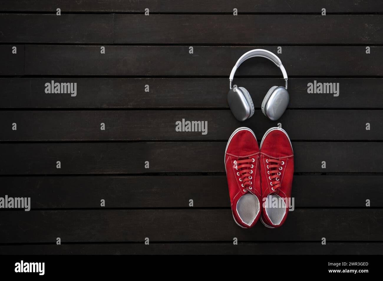 Rote Sneakers mit Kopfhörern auf brauner Planke auf der Terrasse eines Penthouse Stockfoto