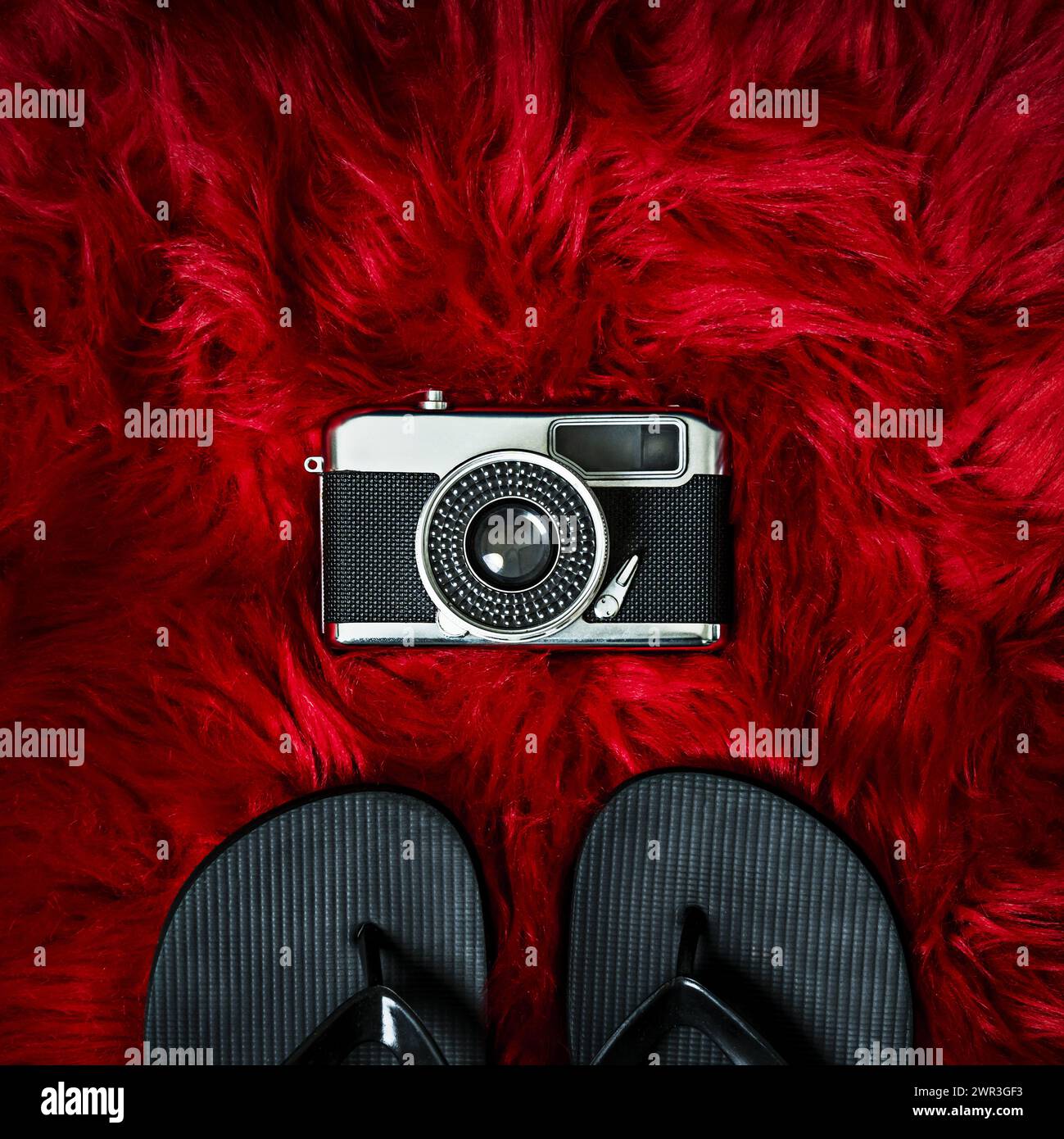 Eine Vintage-Fotokamera neben einem schwarzen Flipflops auf einer roten Haaroberfläche Stockfoto