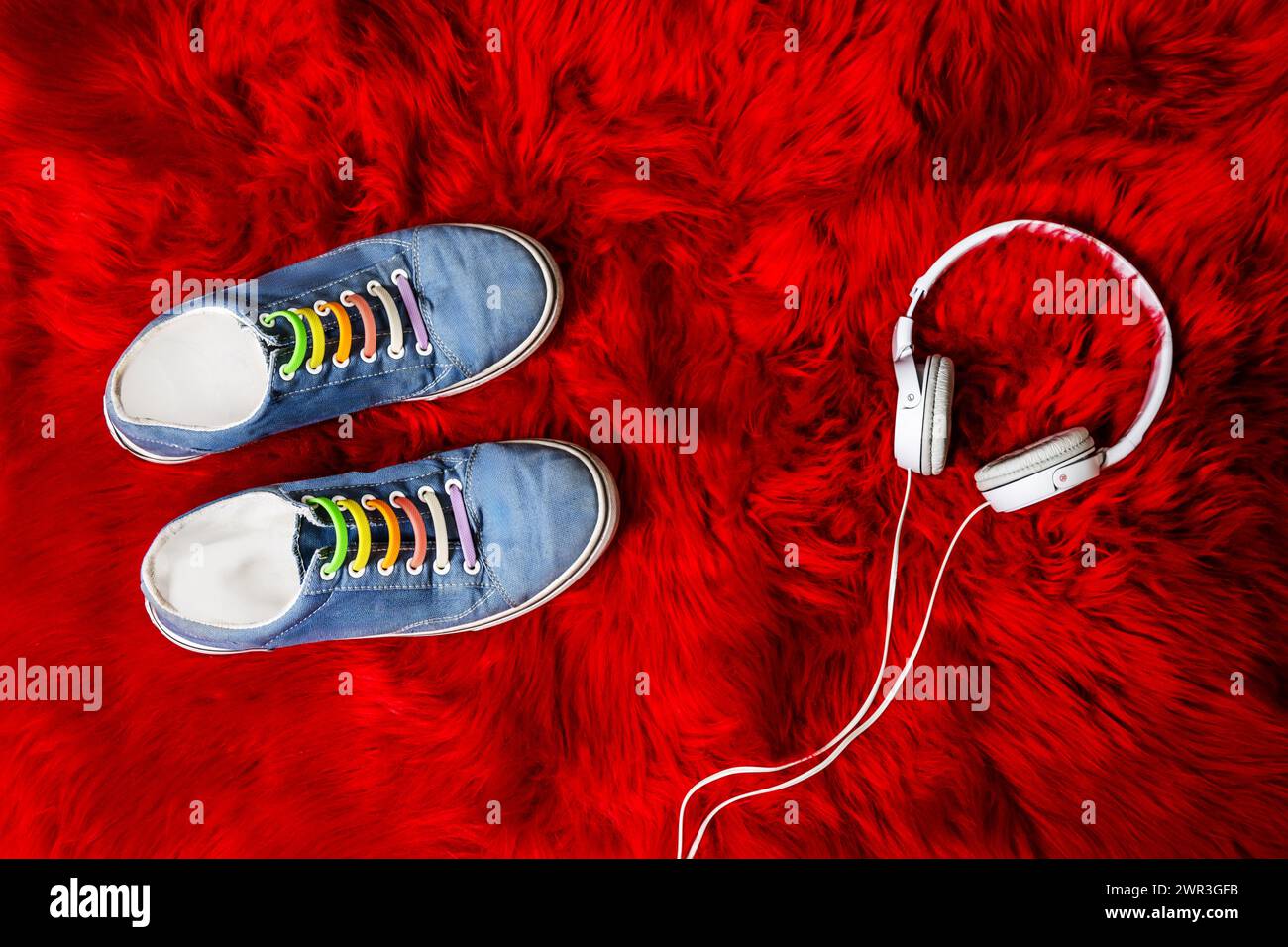 Blaue Sneakers mit weißem Kabelkopfhörer auf roter Felloberfläche Stockfoto