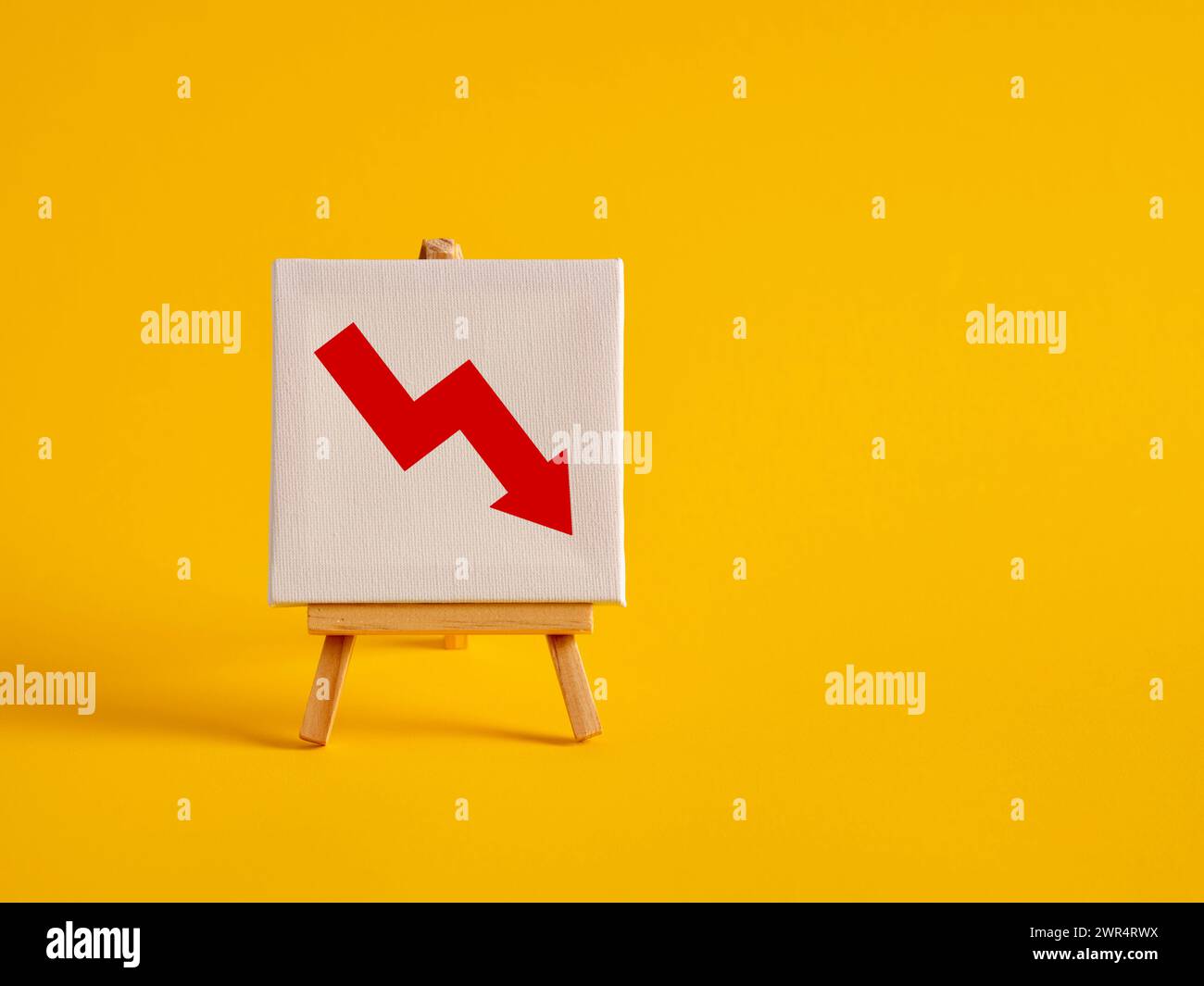 Eine Leinwand mit abnehmendem Diagrammsymbol auf einer Staffelei mit gelbem Hintergrund und Kopierraum. Umsatzrückgang oder -Gewinn. Wirtschaftskrise, Wirtschaftskrise Stockfoto