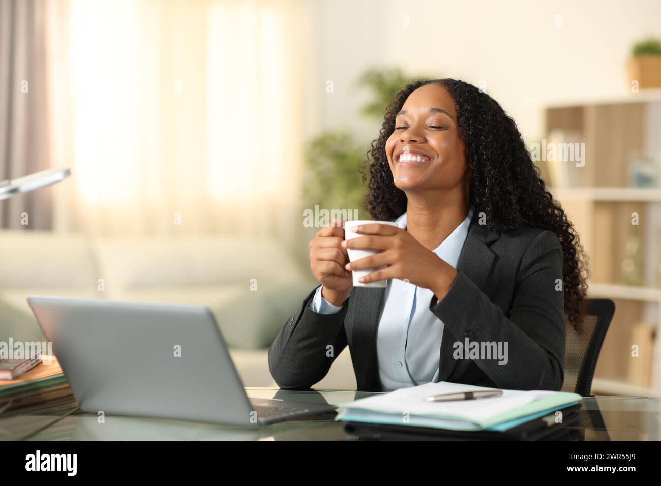 Glücklicher schwarzer Tele-Mitarbeiter, der Kaffee oder Tee trinkt und zu Hause entspannt atmet Stockfoto