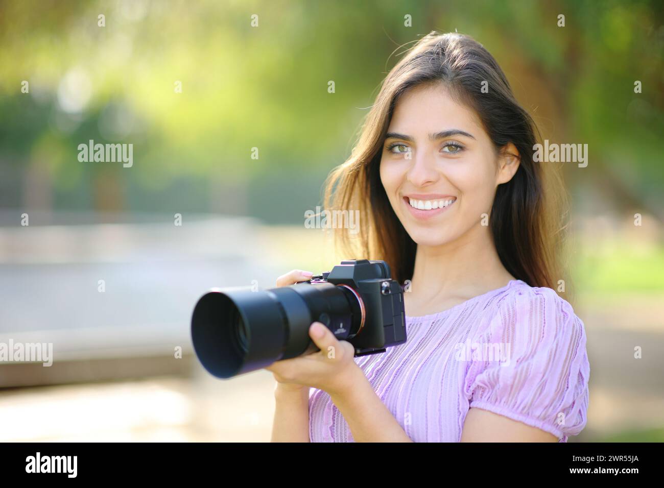 Glücklicher Fotograf posiert in der Kamera und hält spiegellos in einem Park Stockfoto