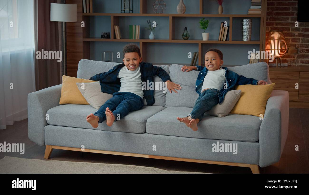 Glückliche Familie zwei adoptierte afroamerikanische ethnische kleine Jungen Kinder Geschwister Kinder ruhen zusammen im Wohnzimmer auf Sofa entspannen lachen lächelnd Stockfoto