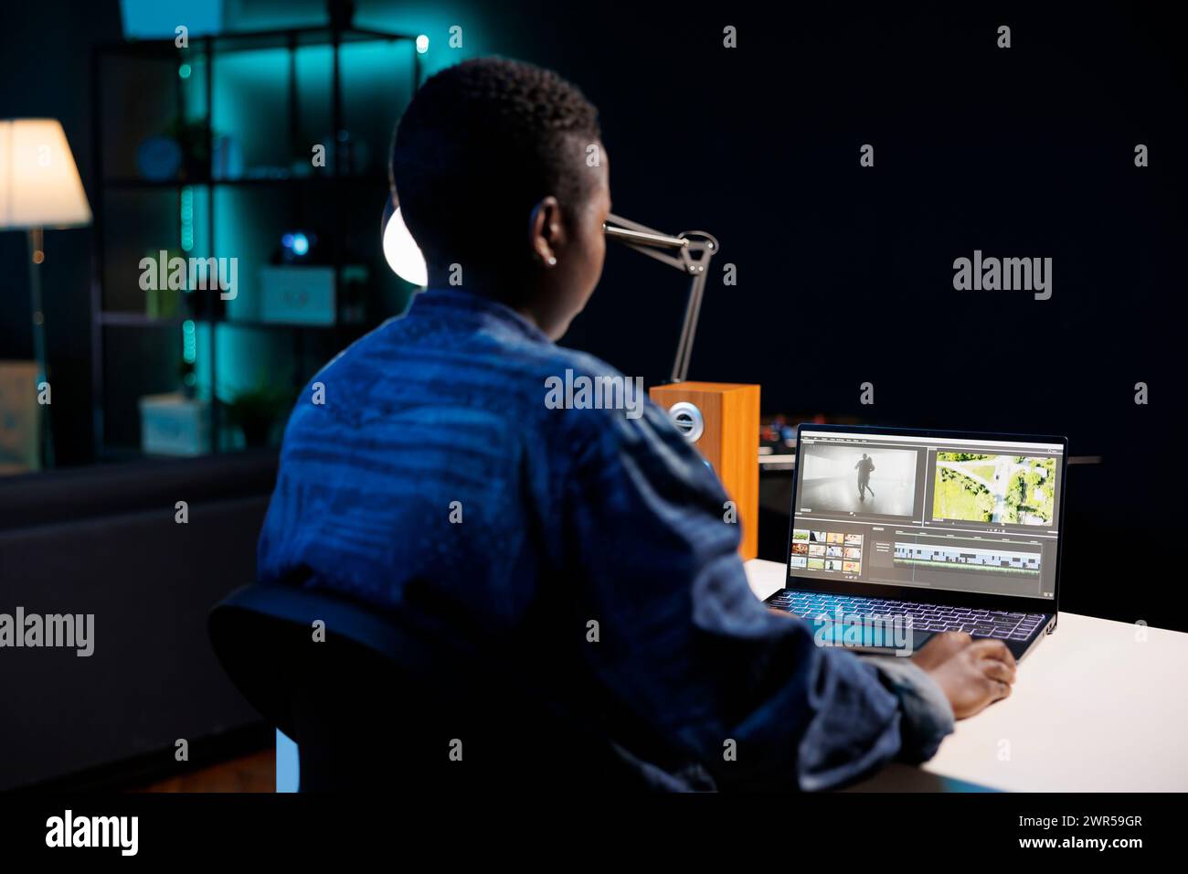 Die afroamerikanische Filmemacherin vertieft sich in ihren PC, bearbeitet und erstellt Multimedia-Inhalte. Das Bild zeigt eine schwarze Frau, die auf einem digitalen Laptop sitzt und arbeitet und das Filmmaterial analysiert. Stockfoto