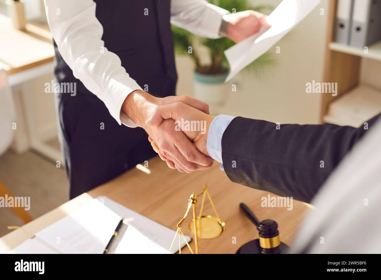Männlicher Anwalt schüttelt Hand mit einem männlichen Mandanten, der am Schreibtisch im Büro steht. Stockfoto