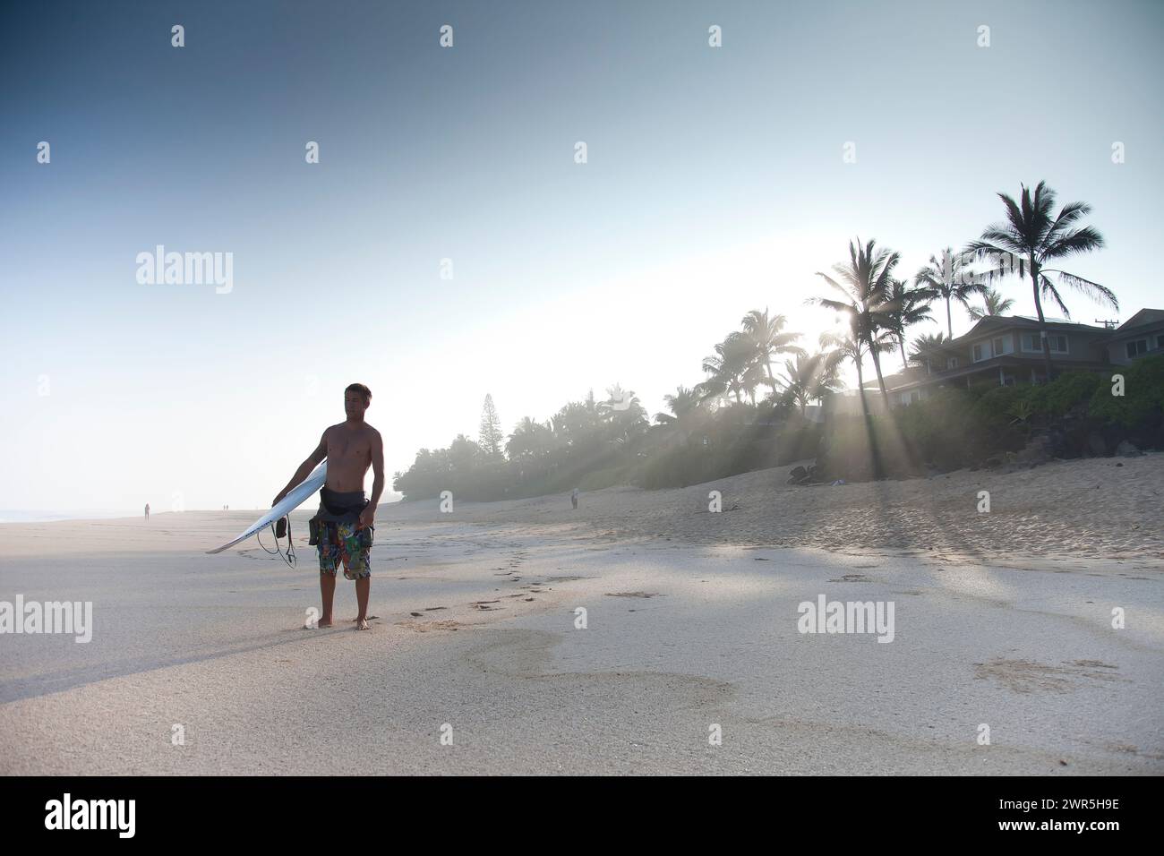 Ein junger Mann, der an einem verlassenen Strand steht und im Begriff ist, surfen zu gehen. North Shore, Oahu, Hawaii Stockfoto