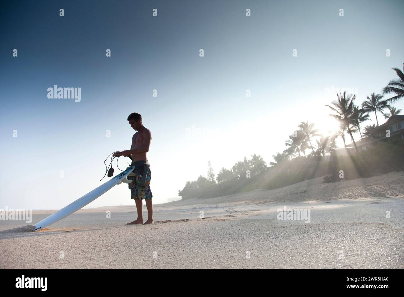 Ein junger Mann, der an einem verlassenen Strand steht und im Begriff ist, surfen zu gehen. North Shore, Oahu, Hawaii Stockfoto