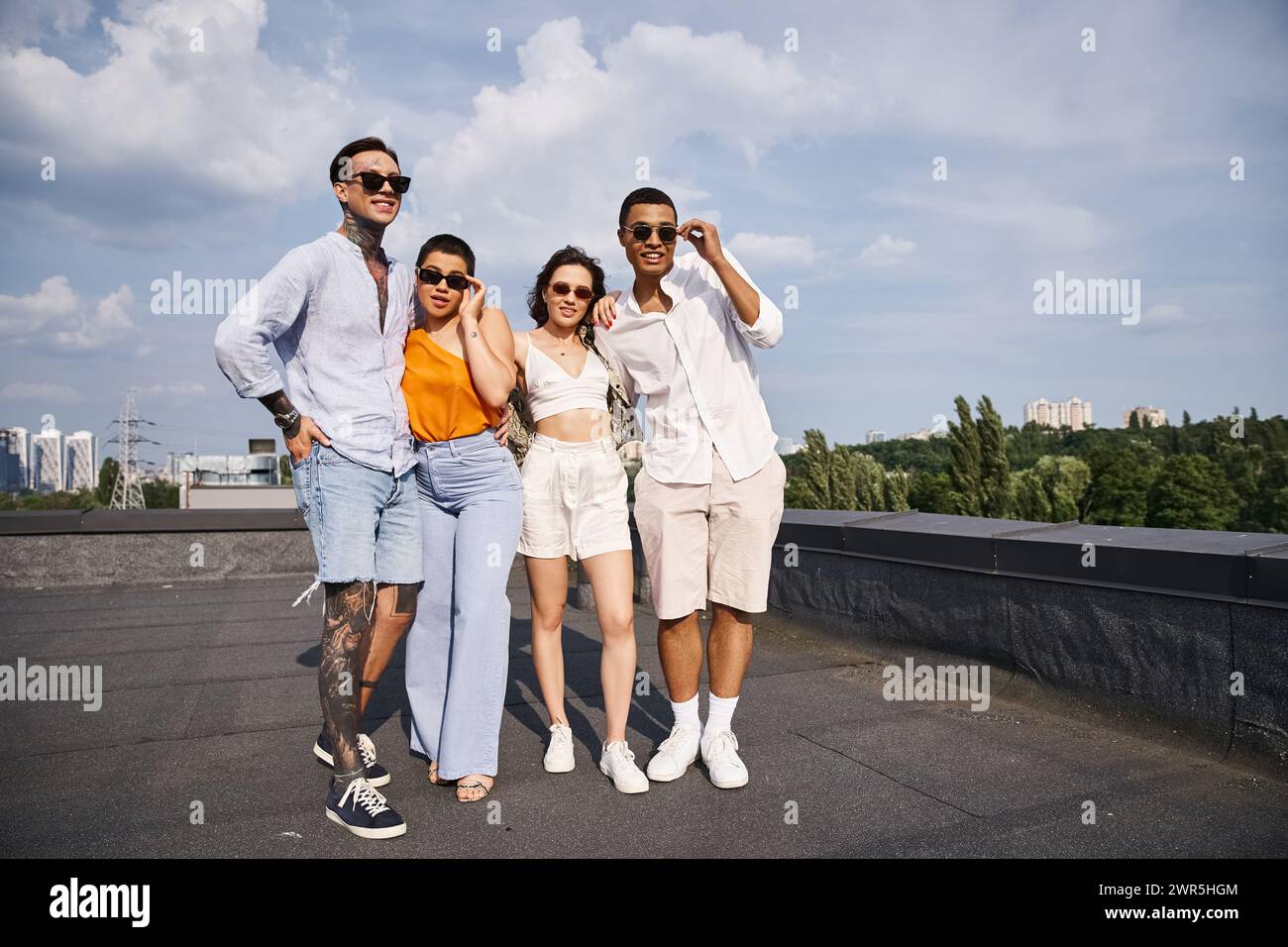 Vier multikulturelle fröhliche Freunde mit moderner Sonnenbrille posieren fröhlich zusammen auf dem Dach Stockfoto