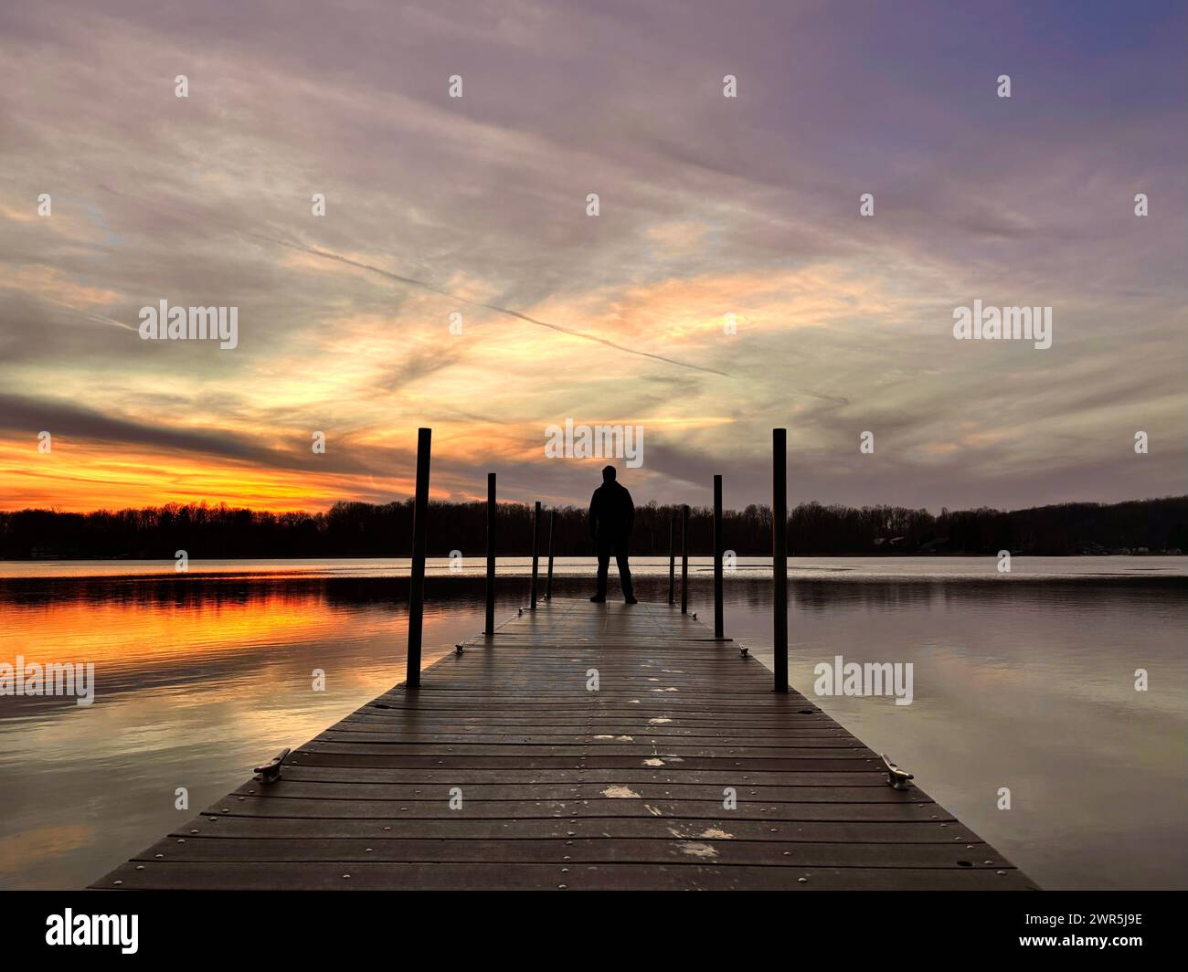 Mann, der auf dem Dock steht und zum See mit Sonnenuntergang starrt Stockfoto