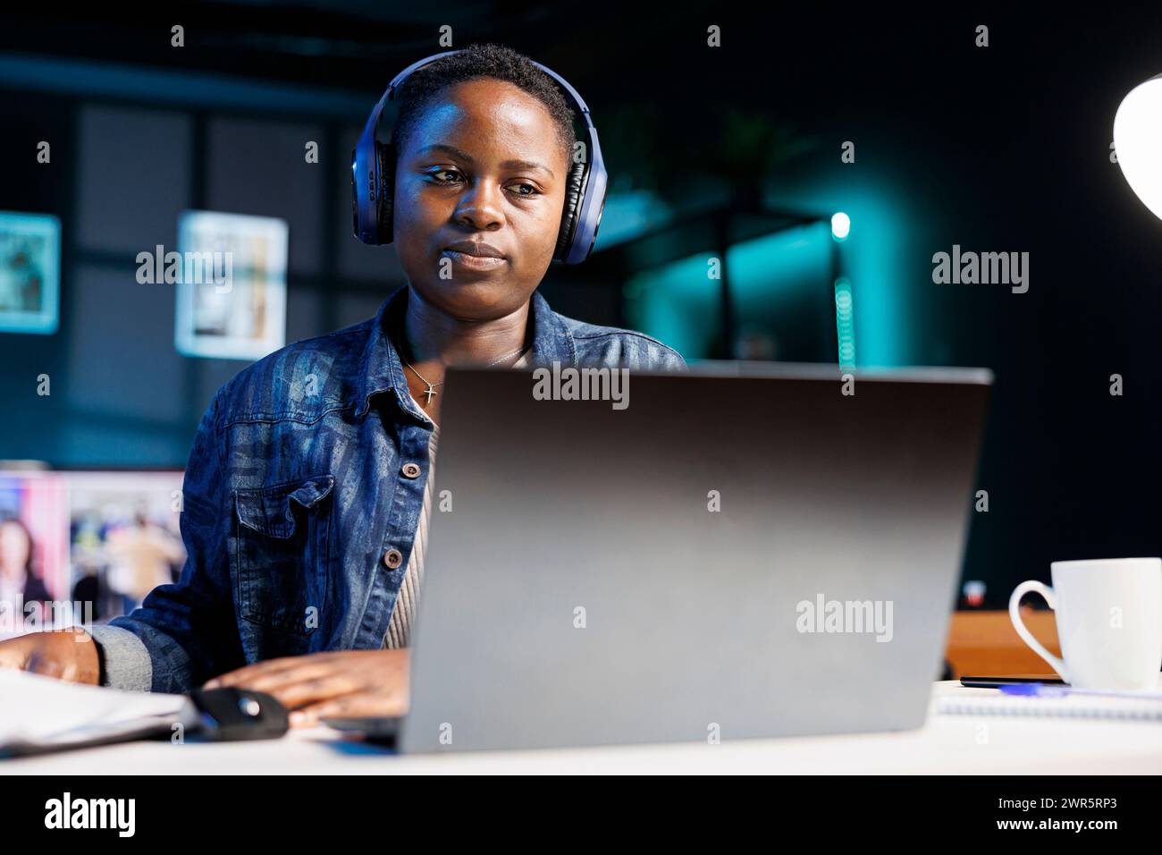 Fokussierte schwarze Frau, die schnurlose Kopfhörer mit Laptop trägt und Notizen schreibt. afroamerikanische Studentin mit Headset, die Online-Webinar ansieht und Audiokurse auf PC anhört. Stockfoto