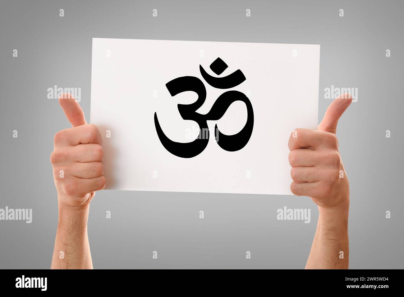 Hände eines religiösen Mannes mit einem OK-Schild, das ein weißes Poster mit gezeichnetem hindu-Symbol mit grauem isoliertem Hintergrund hält Stockfoto