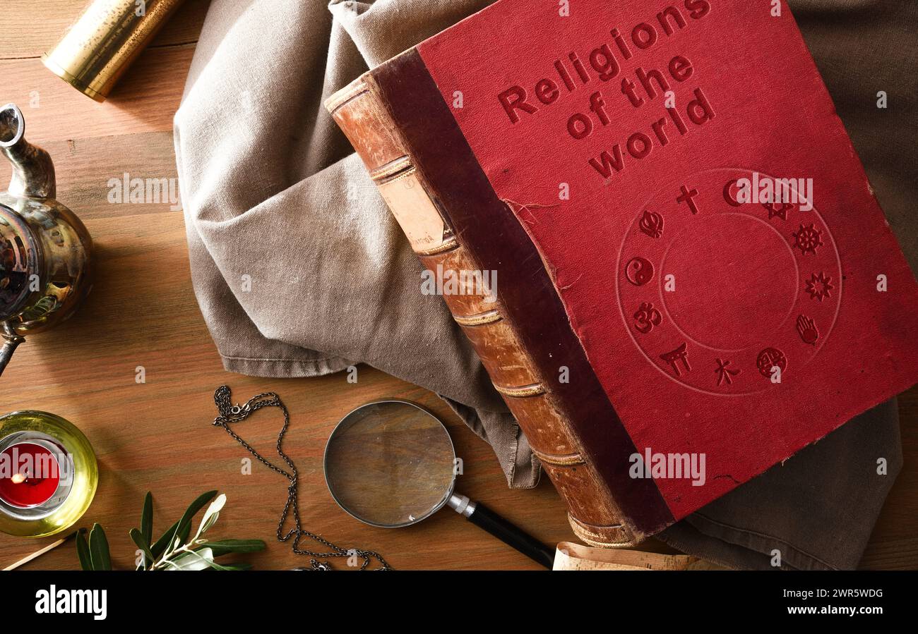 Altes und verschlechtertes Buch der Religionen der Welt mit eingravierten Buchstaben auf dem Cover und antiken Studien- und Abenteuergegenständen auf Holztisch. Stockfoto