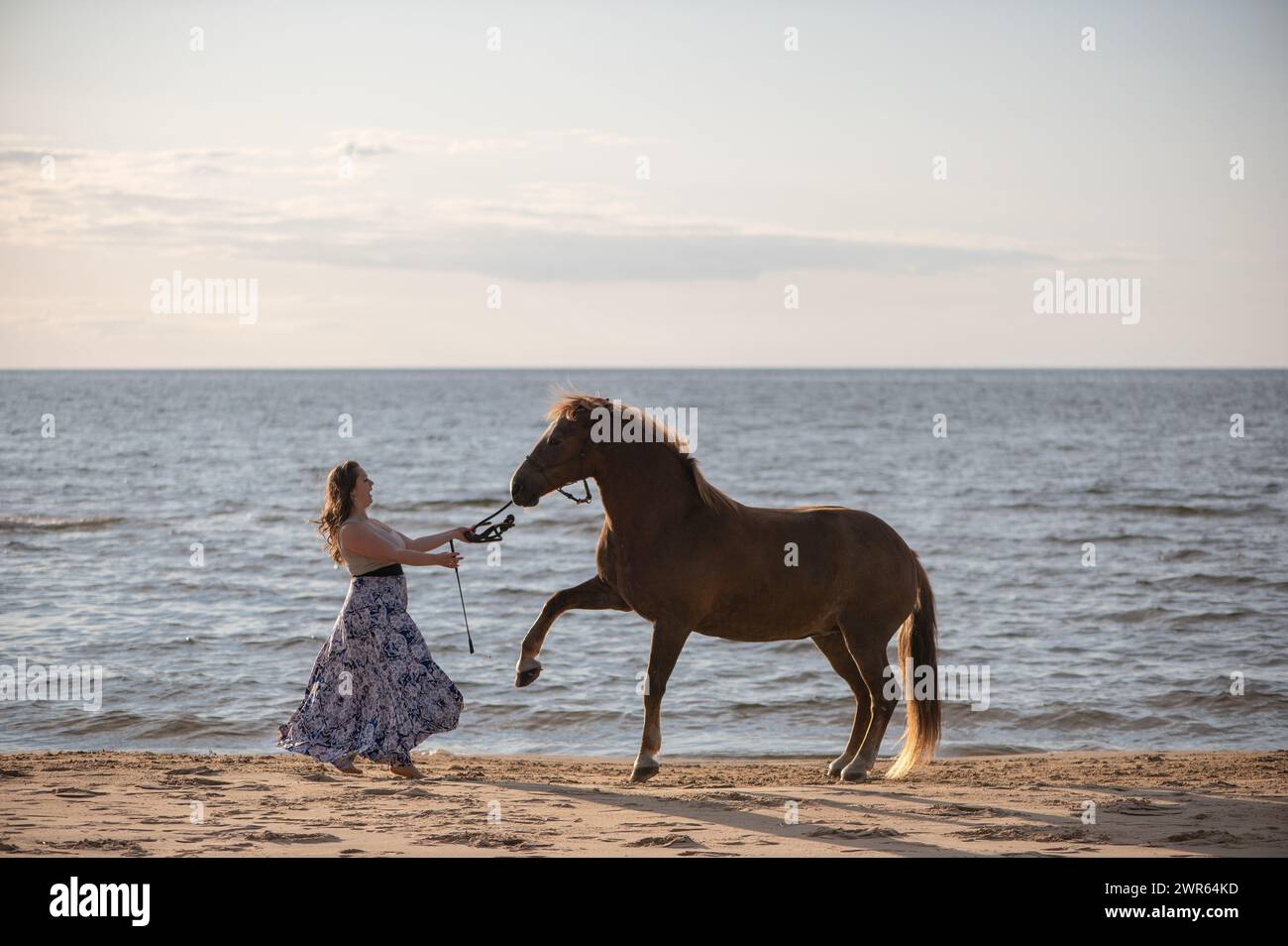 Eine Frau, die am Strand am Wasser ein Pferd streichelt Stockfoto