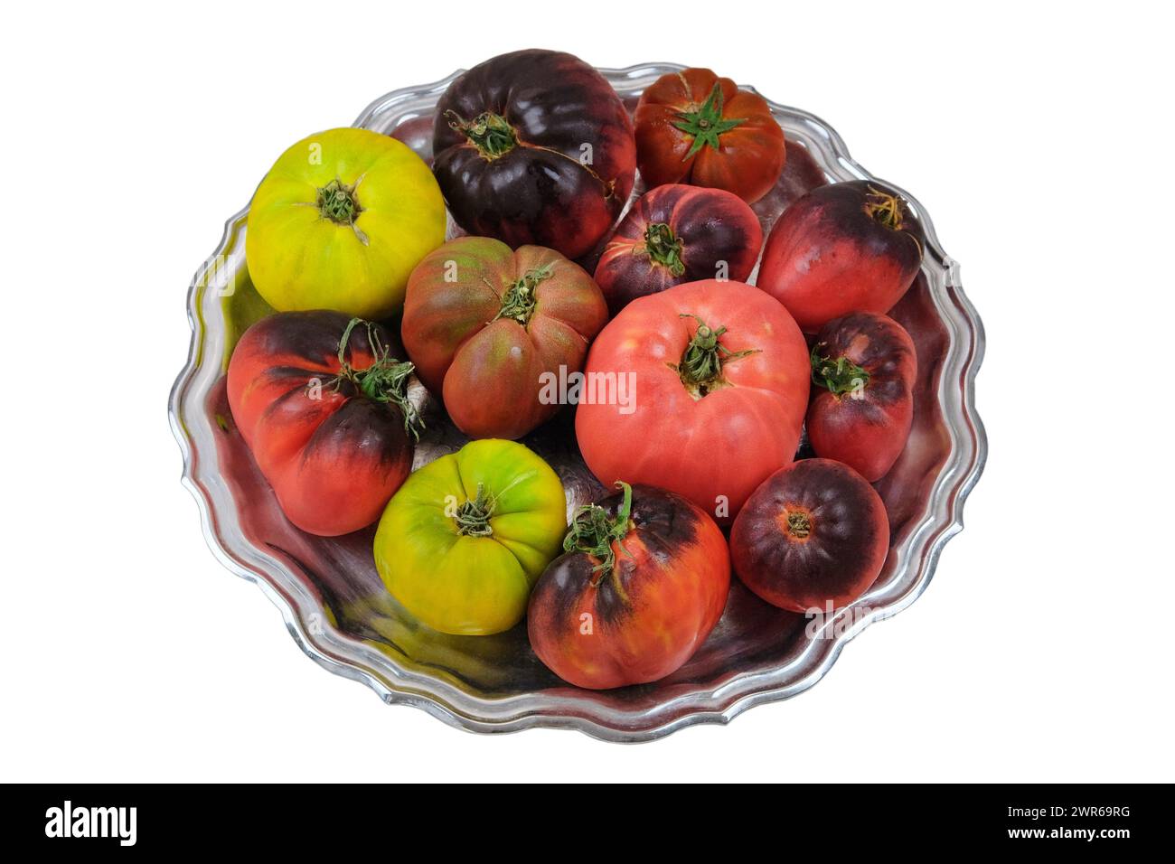Tomaten in einer Metallplatte isoliert auf weißem Hintergrund. Tomatenvielfalt in rustikaler Schüssel. Stockfoto