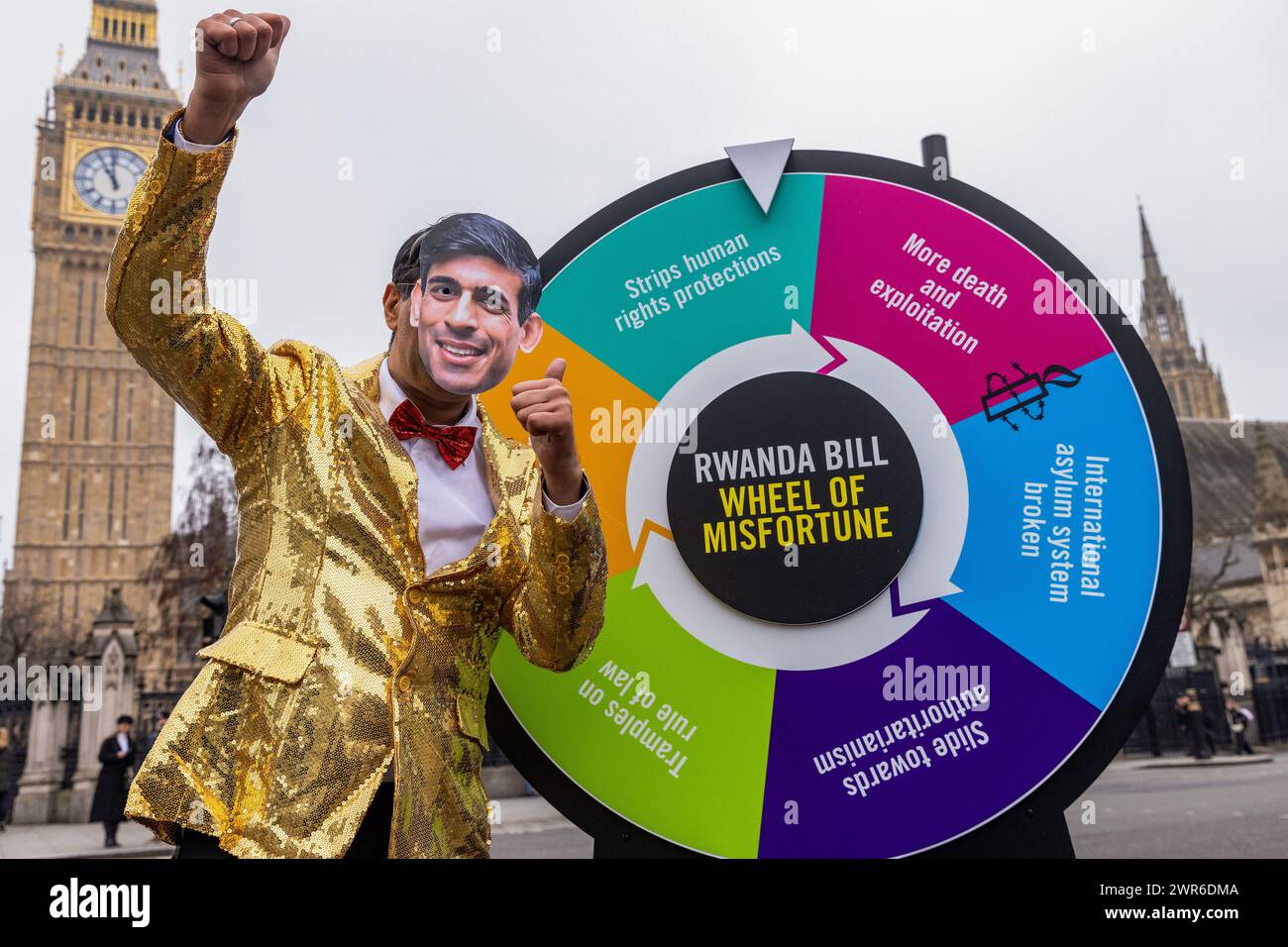 London, Großbritannien. März 2024. Ein Schauspieler, der eine Rishi Sunak Maske trägt und als Gastgeber einer Gameshow gekleidet ist, steht neben einem „Rad des Unglücks“ auf dem Parlamentsplatz während einer Veranstaltung, die von Amnesty International UK inszeniert wurde, um die schwerwiegenden negativen Folgen des Gesetzes zur Sicherheit Ruandas der Regierung hervorzuheben. Das House of Lords wird am 12. März über das umstrittene Gesetz abstimmen, und Amnesty International UK fordert Peers auf, das Gesetz abzulehnen. Quelle: Mark Kerrison/Alamy Live News Stockfoto
