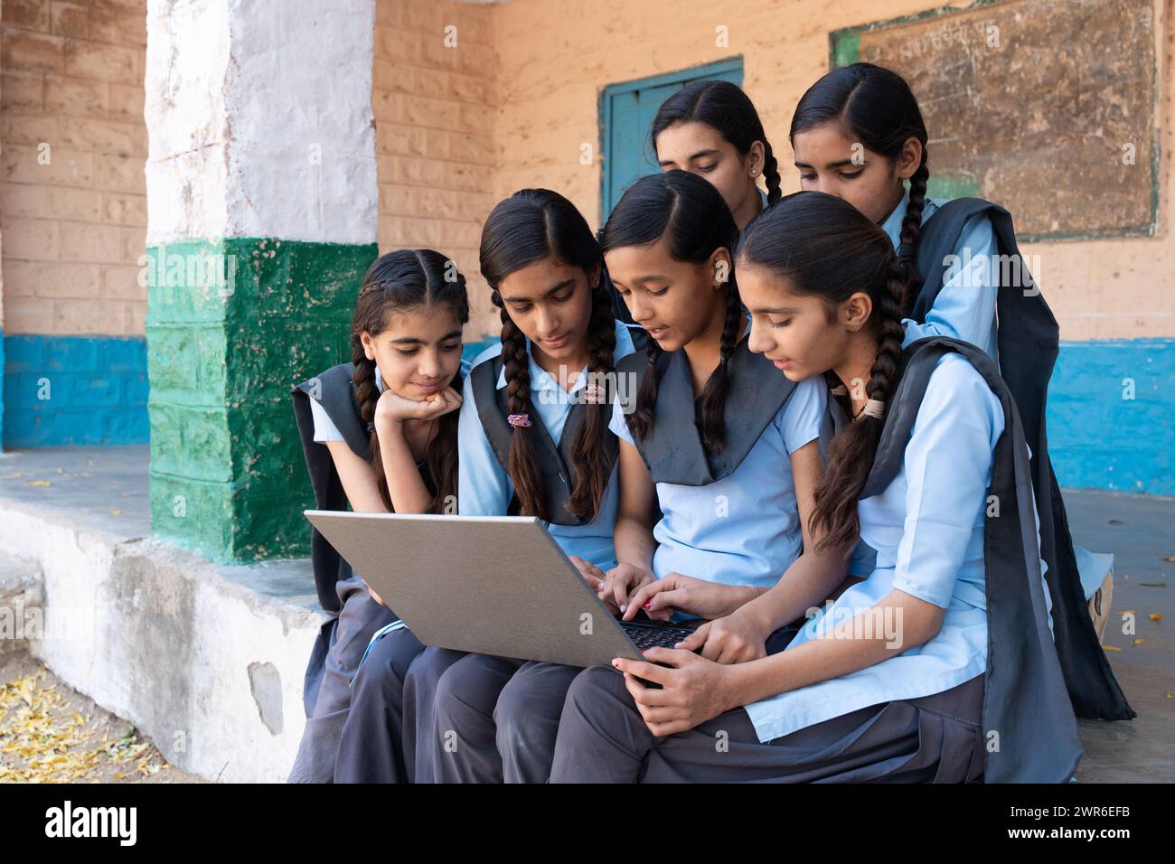 Gruppe ländlicher Schulmädchen in Uniform, die im Schulkorridor sitzen und am Laptop arbeiten - Konzept der digitalen Bildung Stockfoto