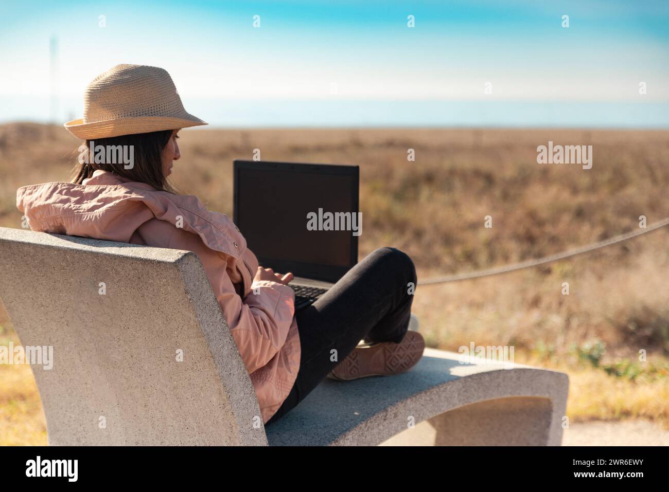 Frau mit Laptop, die vor dem Strand in Barcelona sitzt. Stockfoto