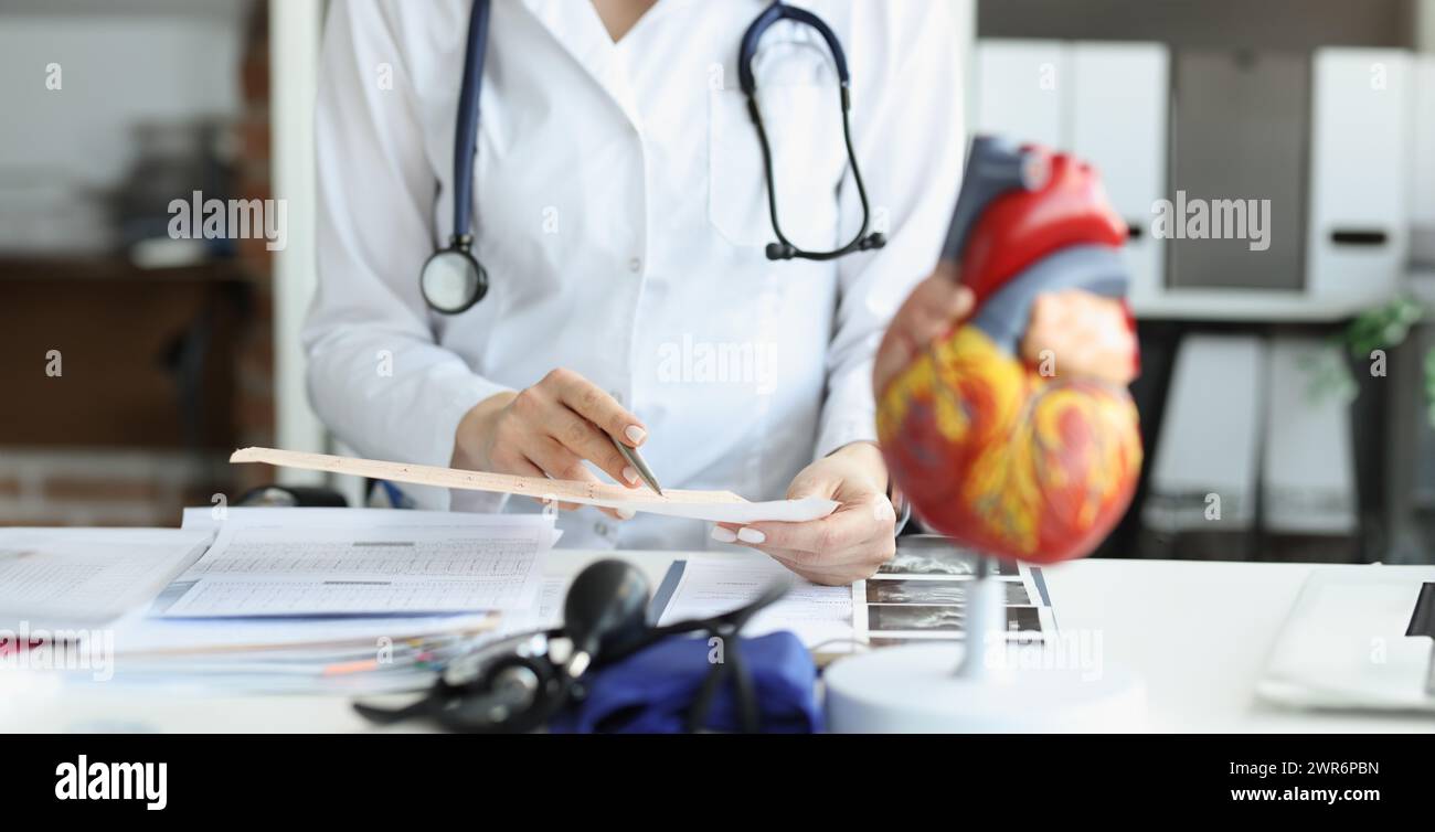 Arzt Kardiologe untersucht Kardiogramm vor dem Hintergrund der künstlichen Herzmodell Nahaufnahme Stockfoto