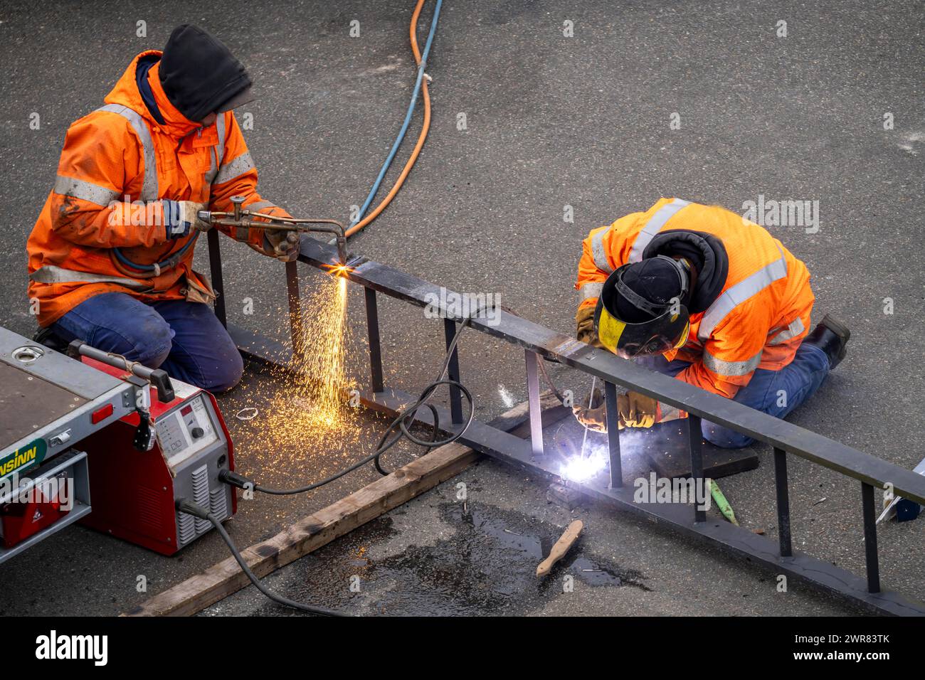 Schlosser bei der Arbeit, beim Schneiden und Schweißen, an einem Werkstück in einem Industriewerk wird eine Metallleiter mit einem Schweißbrenner geteilt, ein Schweißer fixiert eine Leiter r Stockfoto