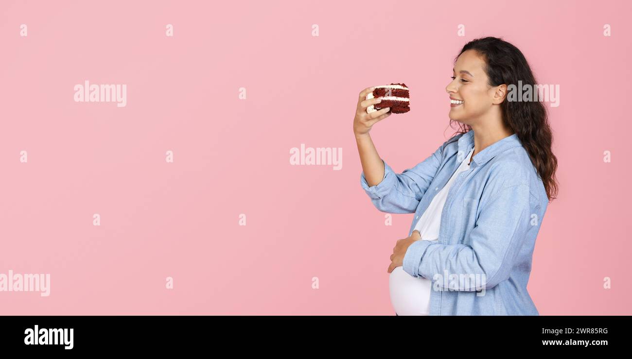 Eine glückliche tausendjährige schwangere Frau, die ein Stück Kuchen hält Stockfoto