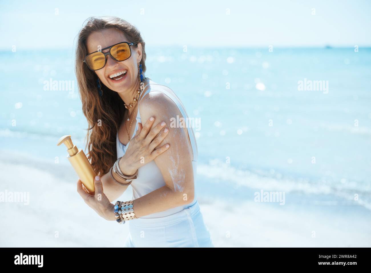 Glückliche moderne Frau am Meer mit Sonnencreme. Stockfoto