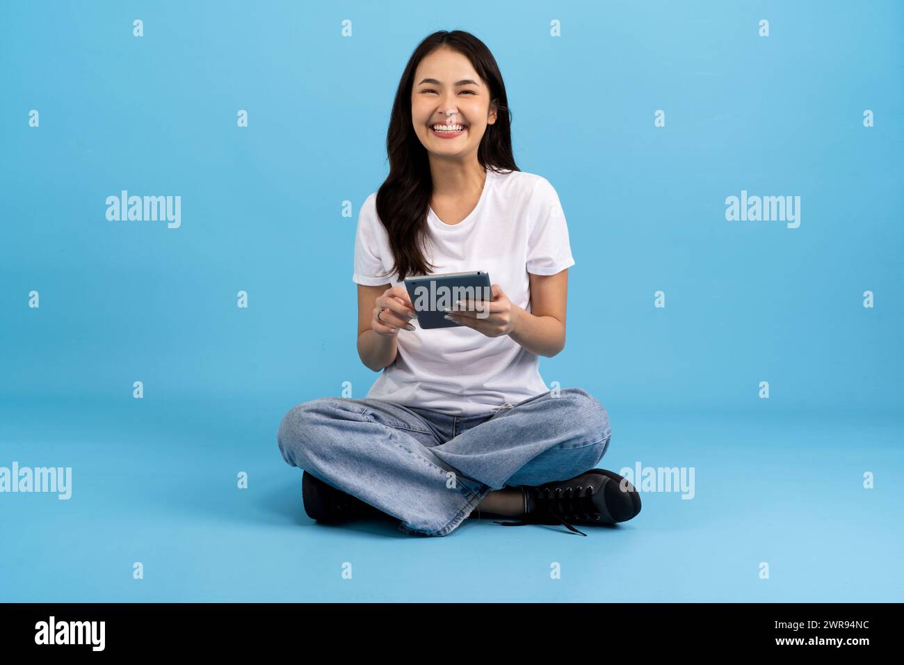 Schönes Mädchen Happy hält Tablet-Computer auf blauem Hintergrund Sitzen und lächeln mit einer entspannten Haltung Genießen Sie das Surfen im Internet mit modernen Geräten Stockfoto