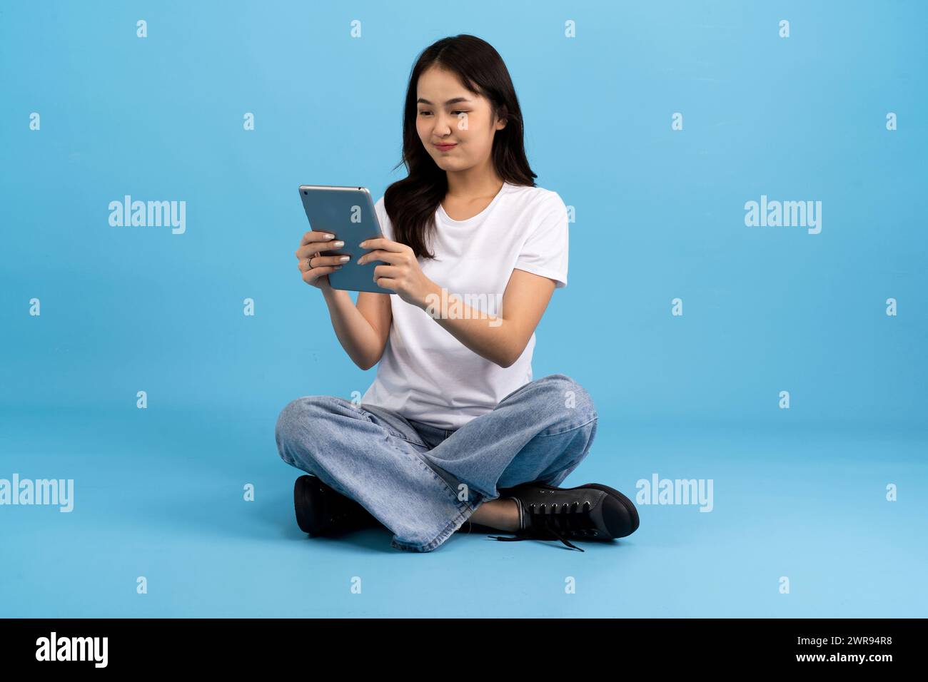 Schönes Mädchen Happy hält Tablet-Computer auf blauem Hintergrund Sitzen und lächeln mit einer entspannten Haltung Genießen Sie das Surfen im Internet mit modernen Geräten Stockfoto