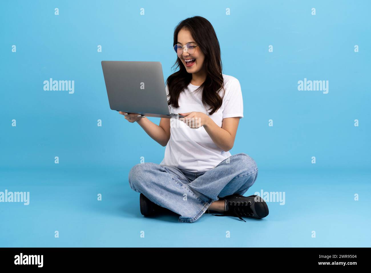 Schönes Mädchen glücklich mit einem Notebook, das auf einem blauen Hintergrund sitzt, sitzen und lächeln mit einer entspannten Haltung Genießen Sie das Surfen im Internet. Stockfoto
