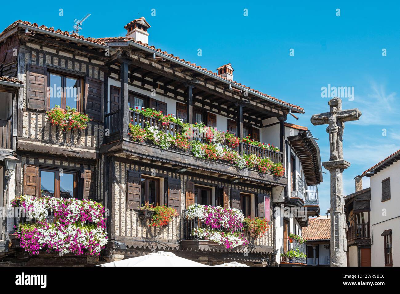 Ein Steinkreuz aus dem 18. Jahrhundert und wunderschöne traditionelle Architektur mit Balkonen, die mit Töpfen geschmückt sind, im mittelalterlichen Dorf La Alberca, Spanien Stockfoto