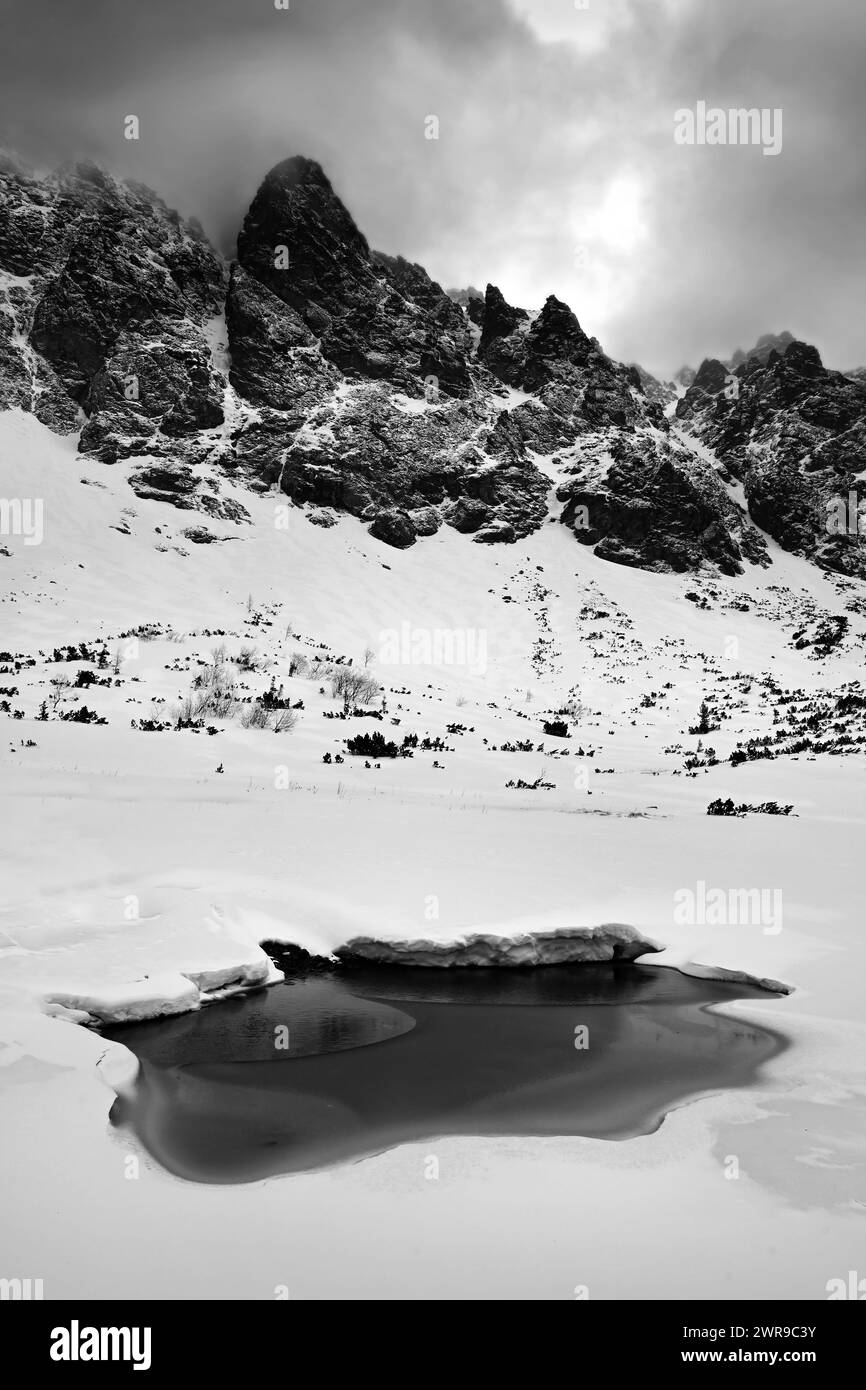 Gefrorener See mit Wasser, umgeben von schneebedeckten Gipfeln in schwarz-weiß in der Nähe von Velické pleso in Velická dolina, oberhalb von Tatranská Polianka, hohe Tatra Stockfoto