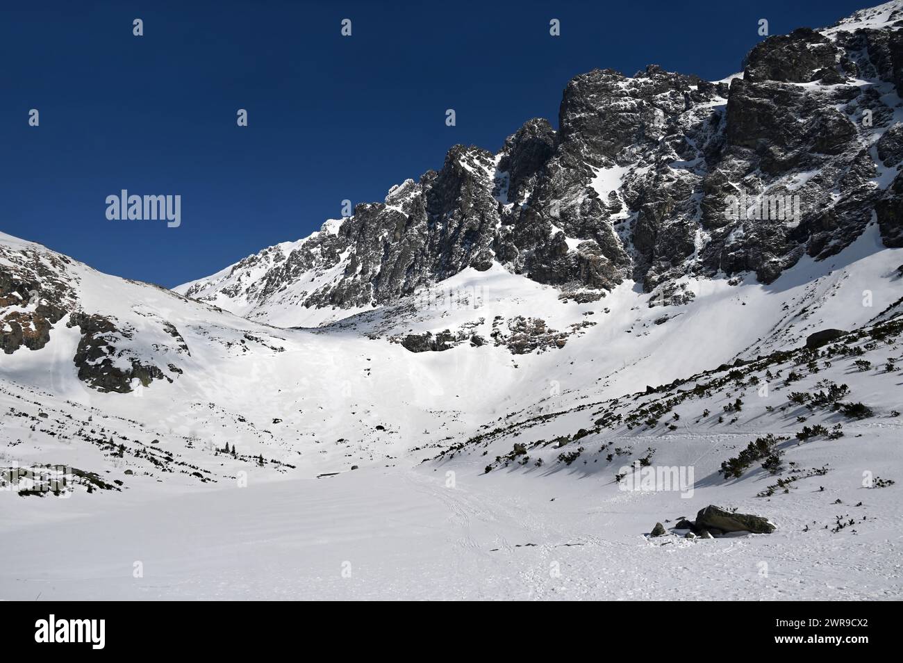 Gefrorener See und schneebedeckte Bergkette unter klarem blauen Himmel in der Nähe von Velické pleso in Velická dolina, oberhalb von Tatranská Polianka, hohe Tatra Stockfoto