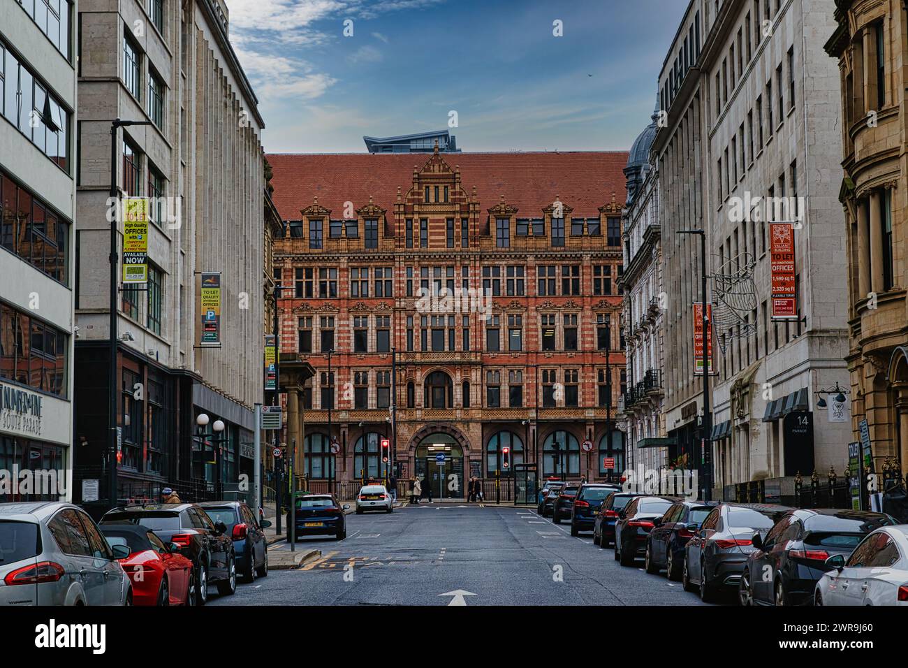 Historische europäische Stadtstraße mit traditioneller Architektur und geparkten Autos unter bewölktem Himmel in Leeds, Großbritannien. Stockfoto