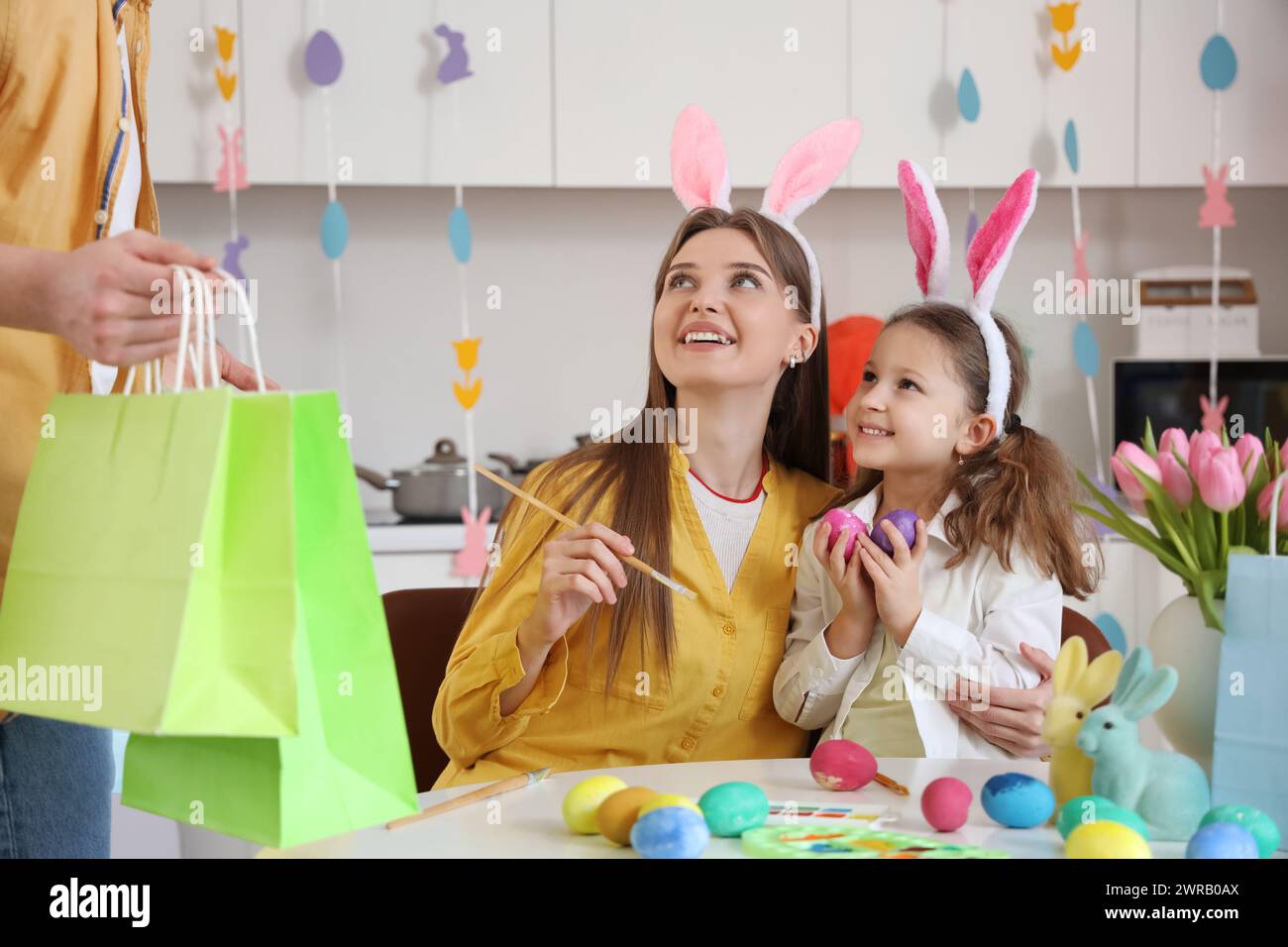 Kleines Mädchen mit ihrer Mutter, das Geschenke vom Vater in der Küche bekommt Stockfoto