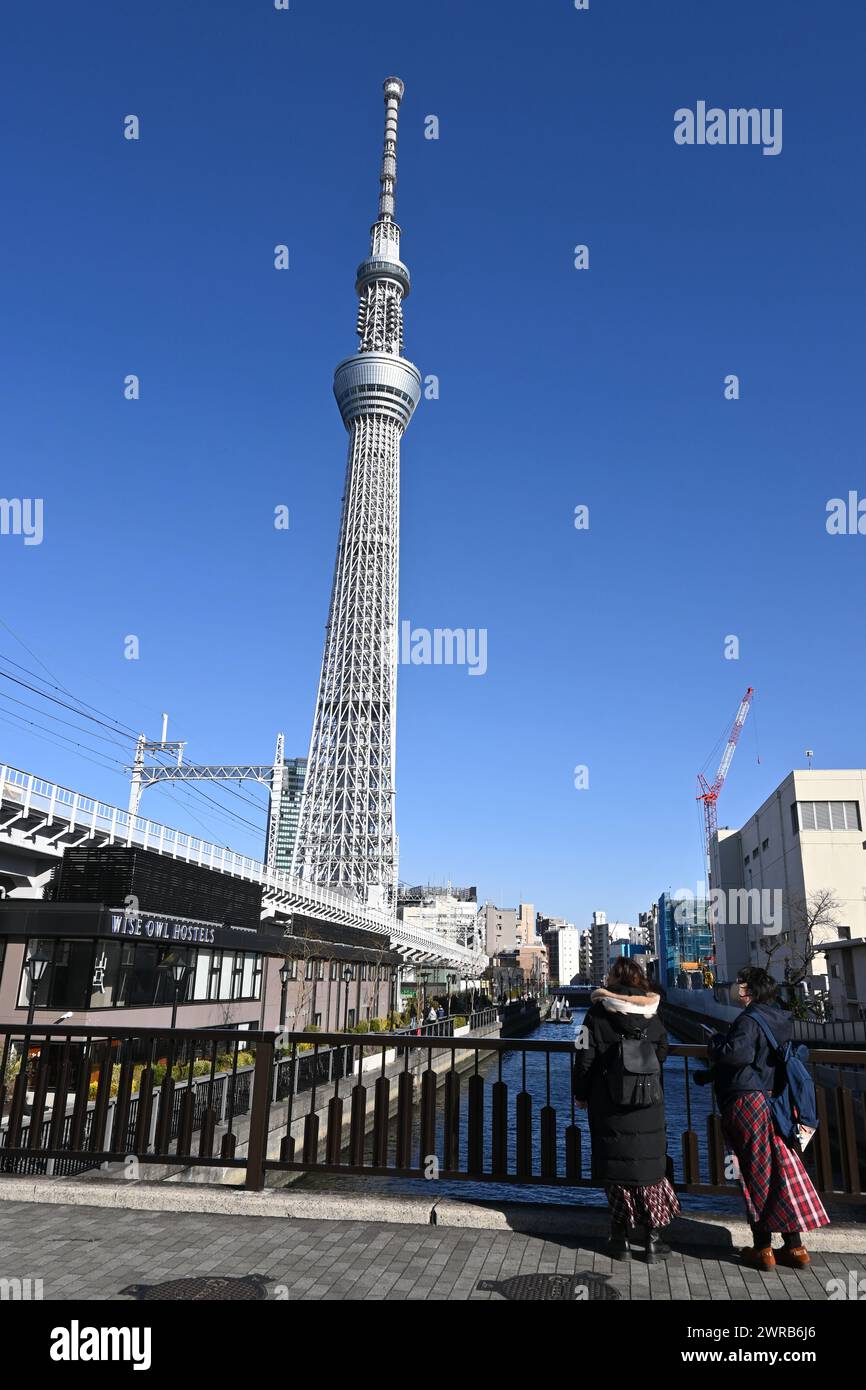 Zwei Menschen blicken an einem sonnigen Tag – Sumida City, Tokio, Japan – von einer Brücke auf den Skytree von Tokio. Am 27. Februar 2024 Stockfoto