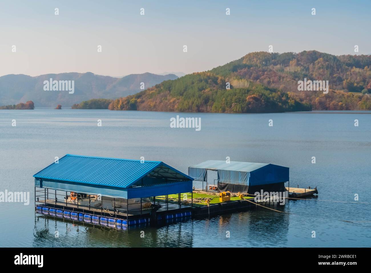 Ein schwimmendes Gebäude mit blauem Dach auf einem ruhigen See mit Bergen in der Ferne, in Südkorea Stockfoto