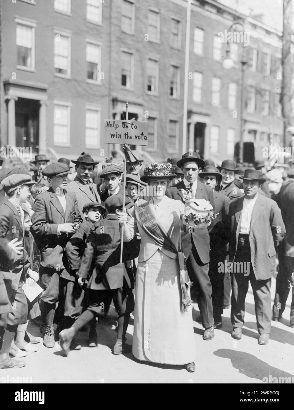 Mrs. Suffern mit einem hausgemachten Banner bei der Parade. Das Foto zeigt Mrs. Suffern, die einen Schärpe trägt und ein Schild trägt, auf dem steht: "Hilf uns, die Stimme zu gewinnen", umgeben von einer Menge von Männern und Jungen., 1914., Frauenwahlrecht, 1910-1920, Fotoabdrücke, 1910-1920., Fotodrucke, 1910-1920, 1 Fotodruck Stockfoto