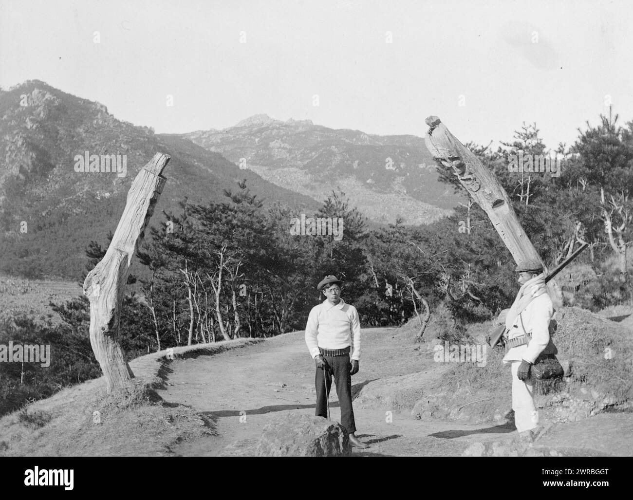 Korea. Pfosten entlang der Straße, die gemeißelt wurden, um Teufel daran zu hindern, das Foto zeigt zwei Männer mit Gewehren und Munitionsgürteln, die zwischen zwei geschnitzten Pfosten auf einer Bergstraße stehen., Carpenter, Frank G. (Frank George), 1855-1924, Fotograf, zwischen 1920 und 1927, Koreaner, Männer, 1920-1930, Fotodrucke, 1920-1930., Fotodrucke, 1920-1930, 1 Fotodruck Stockfoto