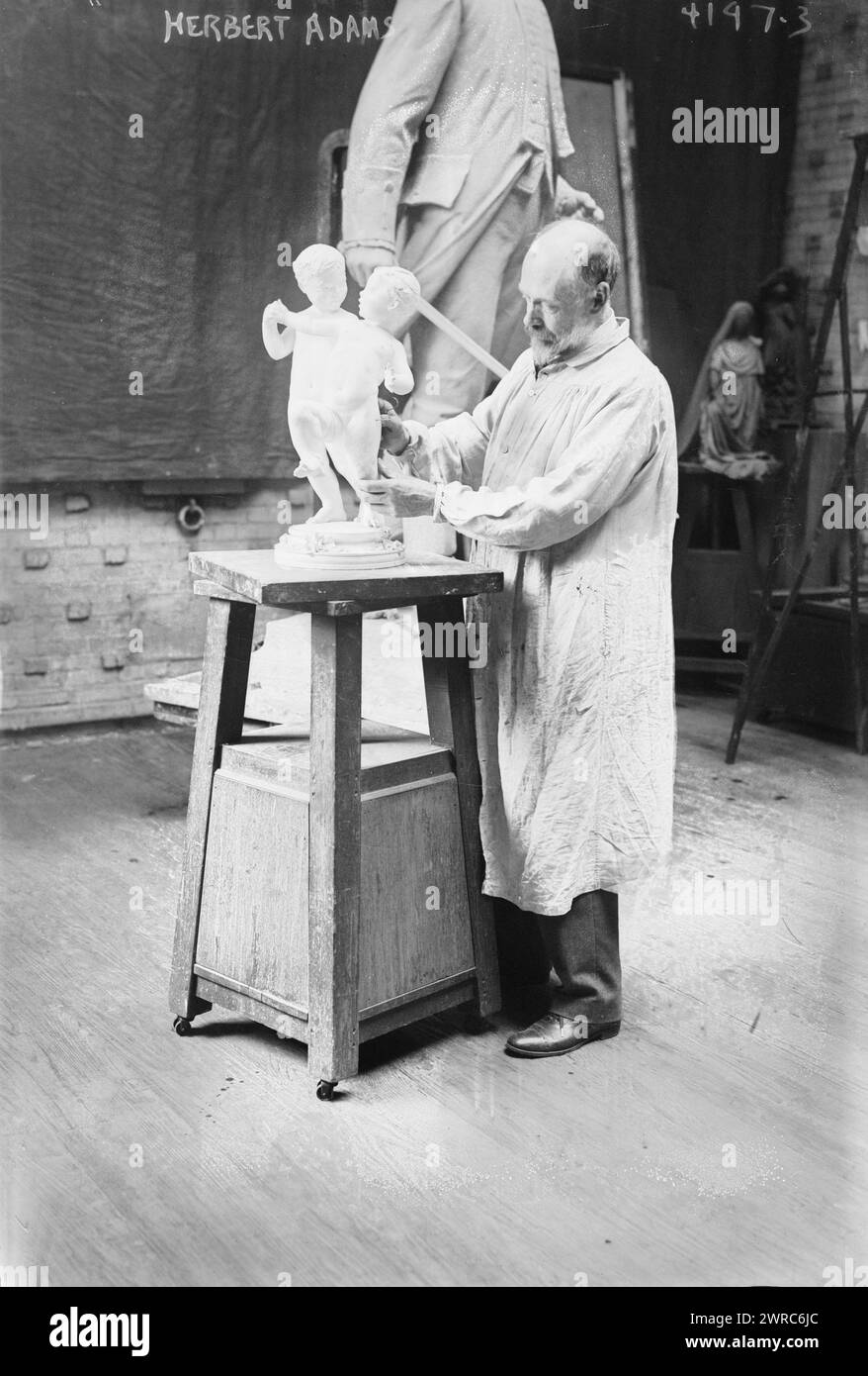 Herbert Adams, Foto zeigt den Bildhauer Samuel Herbert Adams (1858–1945), der an einer Skulptur zweier Kinder arbeitet. Ein Modell einer Skulptur von Loammi Baldwin ist hinter ihm., 2. Mai 1917, Glasnegative, 1 negativ: Glas Stockfoto