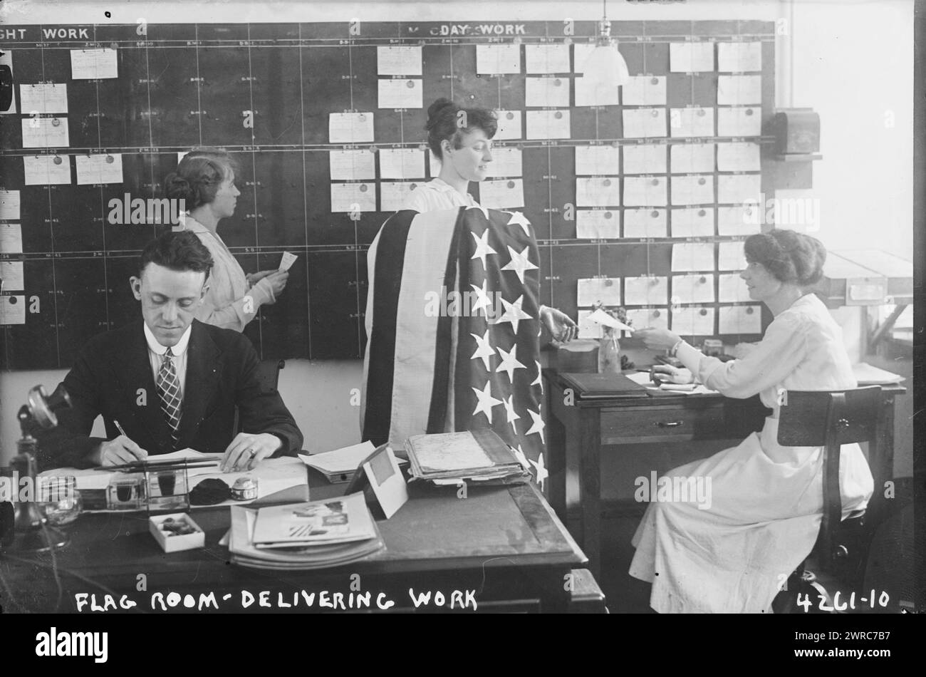 Fahnenraum, Arbeit, Foto zeigt einen Mann und eine Frau, eine mit amerikanischer Flagge, die in einem Büro auf der Brooklyn Navy Yard, Brooklyn, New York, arbeiten. 7. Juli 1917, Glass negative, 1 negativ: Glas Stockfoto