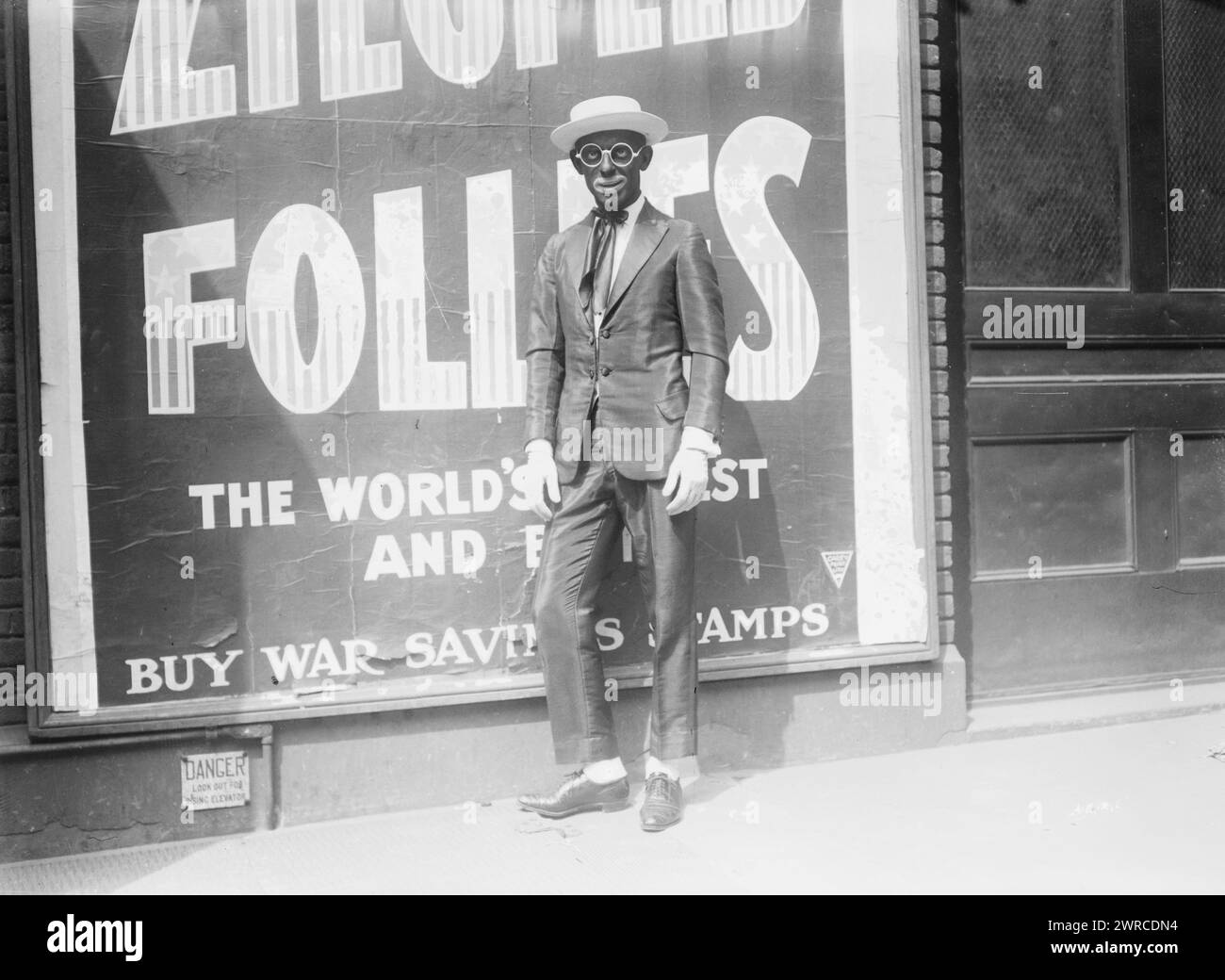 Cantor, Foto zeigt Sänger Eddie Cantor (1892–1964) in schwarzem Gesicht vor einer Werbetafel für die Ziegfield Follies mit 'Buy war Saving Stamps'-Aussage., zwischen 1917 und ca. 1920, Glasnegative, 1 negativ: Glas Stockfoto