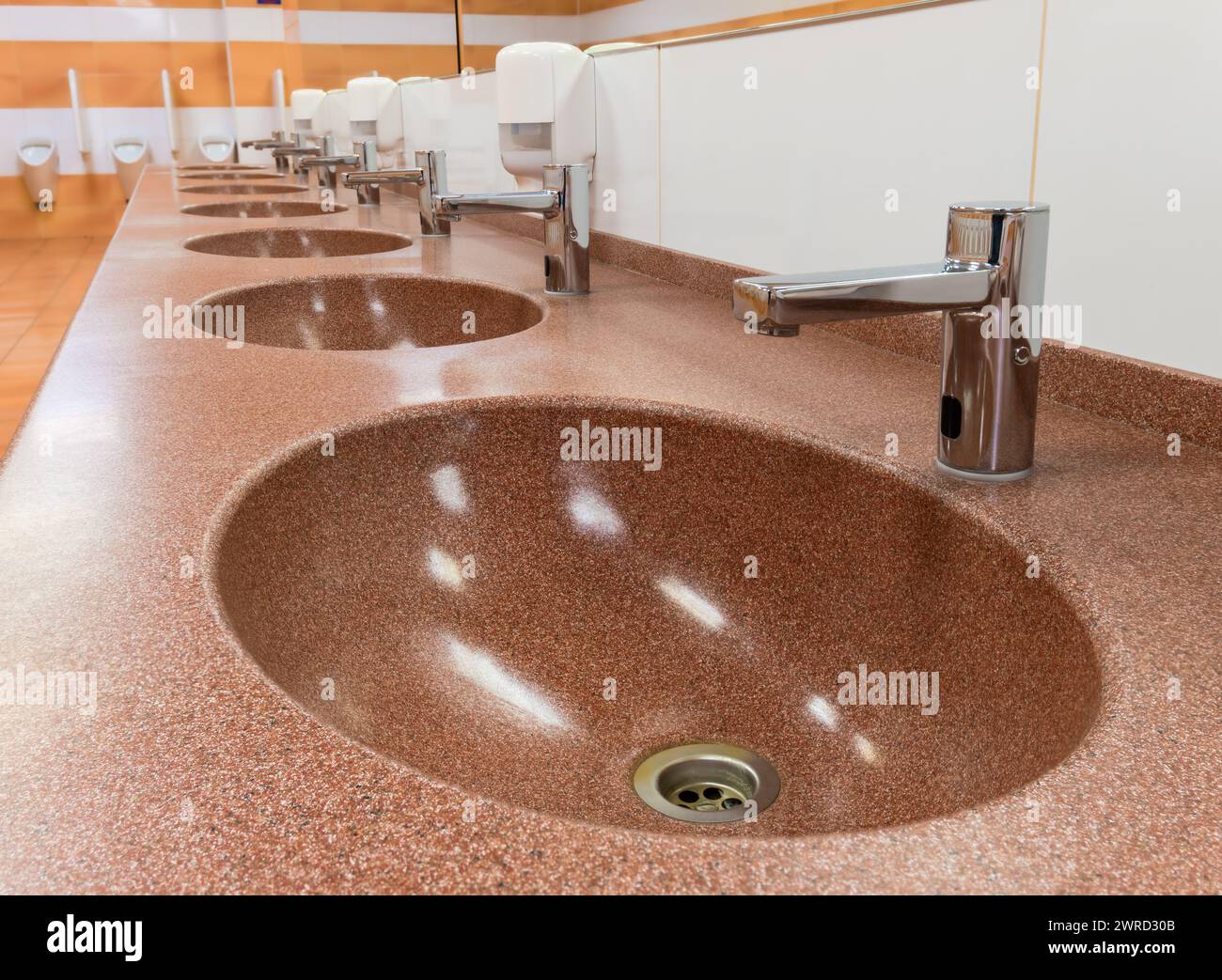 Reihe von Waschtischen mit automatischen Armaturen und Keramikwaschbecken in einer öffentlichen Toilette Stockfoto