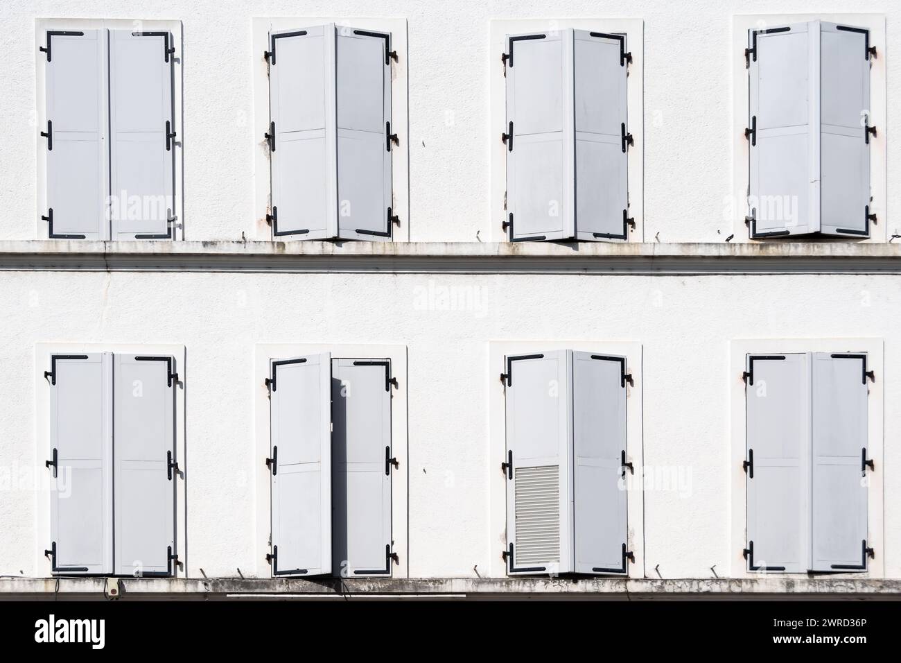 Acht Fenster mit geschlossenen weißen Fensterläden, eines davon offen, an der Fassade eines alten weißen Gebäudes Stockfoto